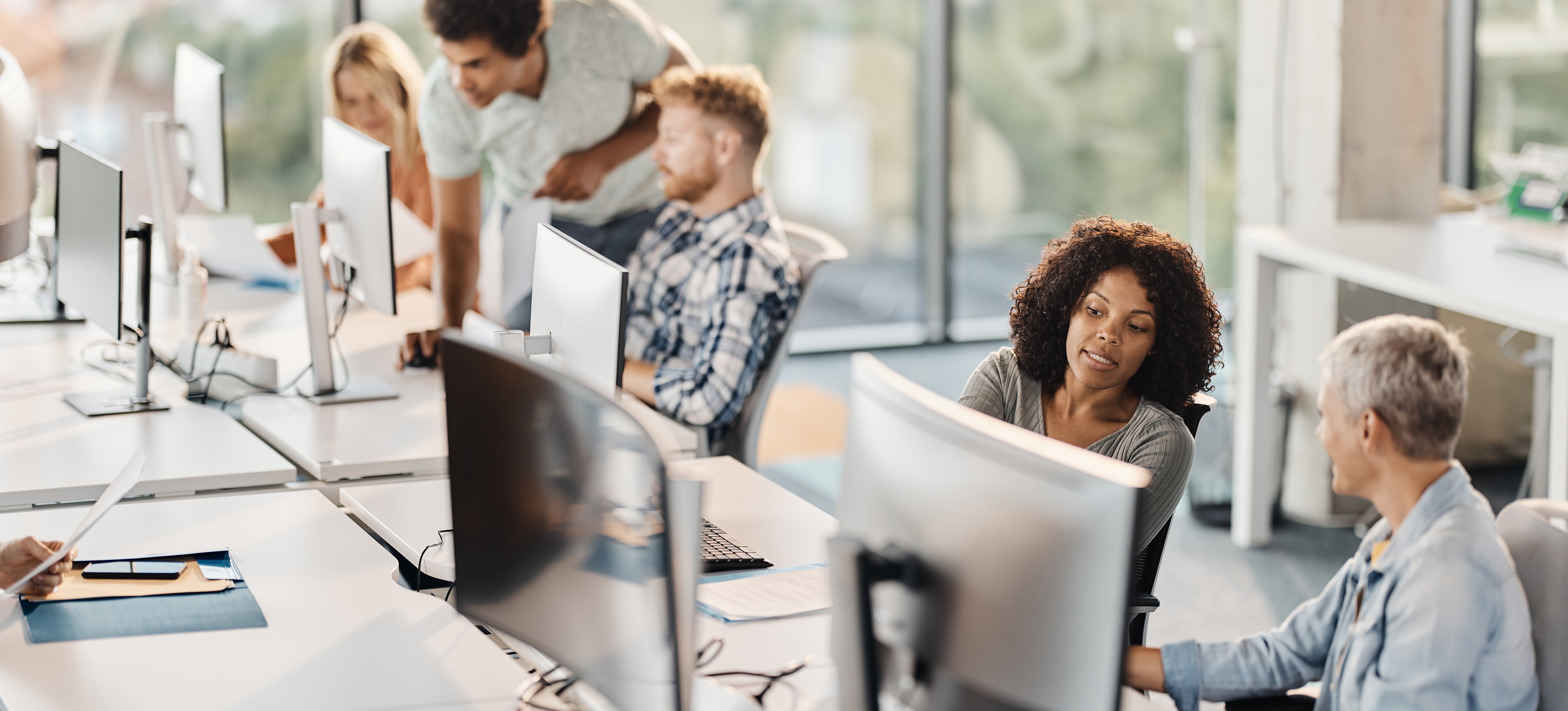 [Hauptbild] Mehrere Kollegen arbeiten an Computerstationen, die in ihrem Bürogebäude über ein lokales Netzwerk verbunden sind.