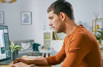 [Featured image] A UX designer in an orange long-sleeve T-shirt works on a prototype on his desktop computer.