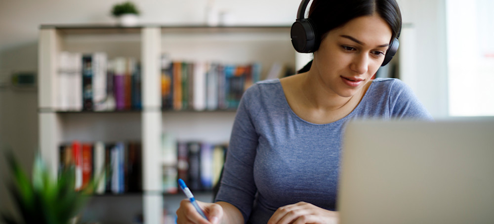 [Featured image] A person pursuing a Bachelor of Applied Science wears over-the-ear headphones while working with a pen and paper in front of their laptop. 
