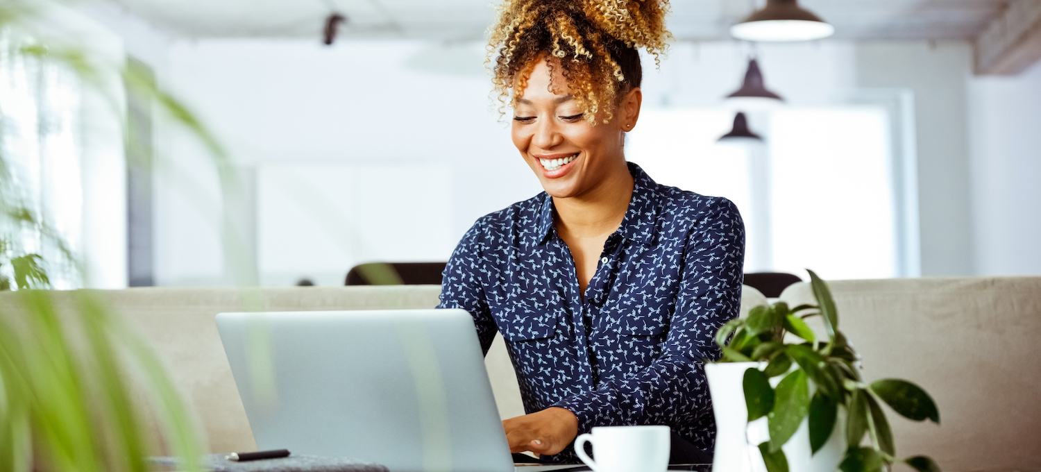 [Featured image] A woman, wearing a long-sleeved blue dress shirt, smiles while writing her resume summary on her laptop. 