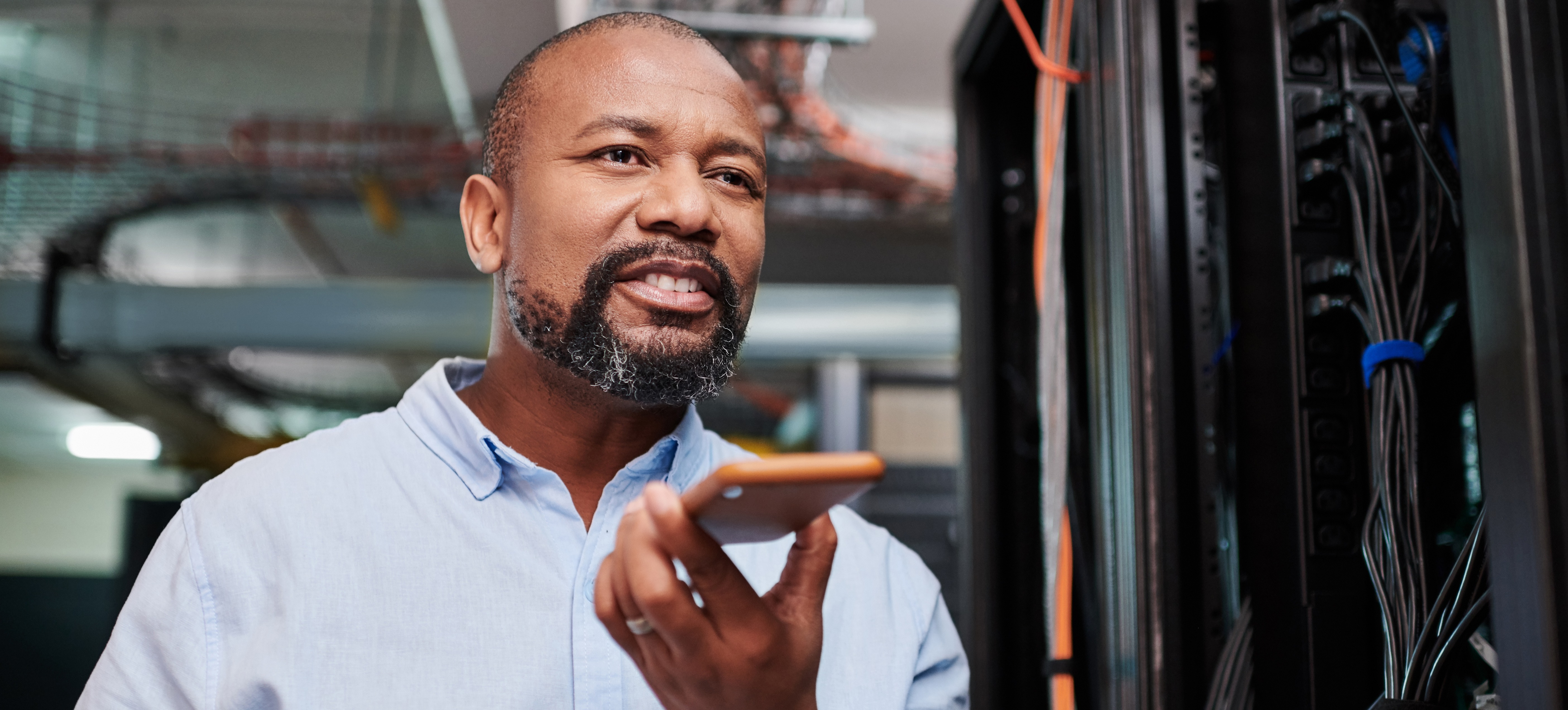 [Featured Image] A man receiving a network technician salary is on a phone call while in a server room.
