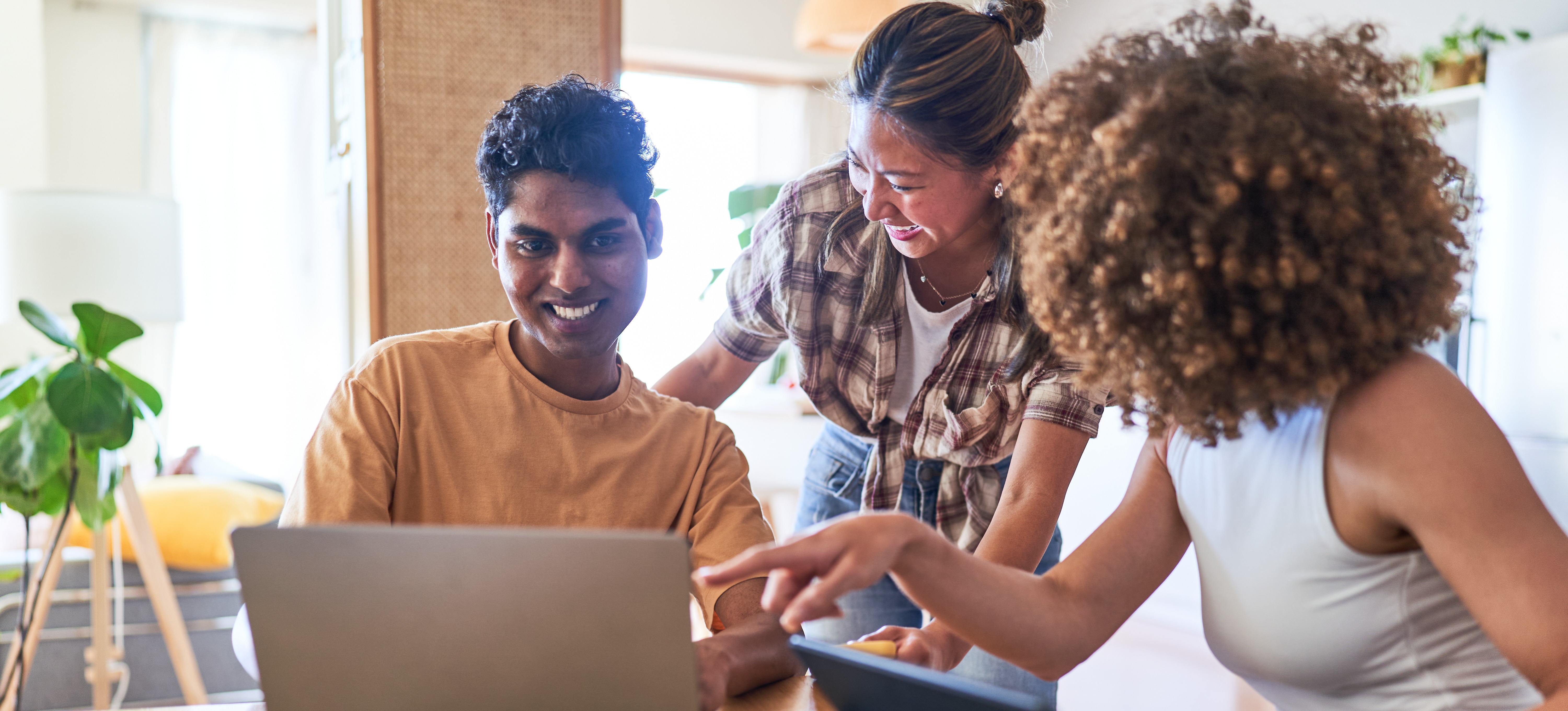[Featured Image] Two learners gather around a third learner who is on their laptop as the trio explore health care data analyst careers and learn about the necessary qualifications. 
