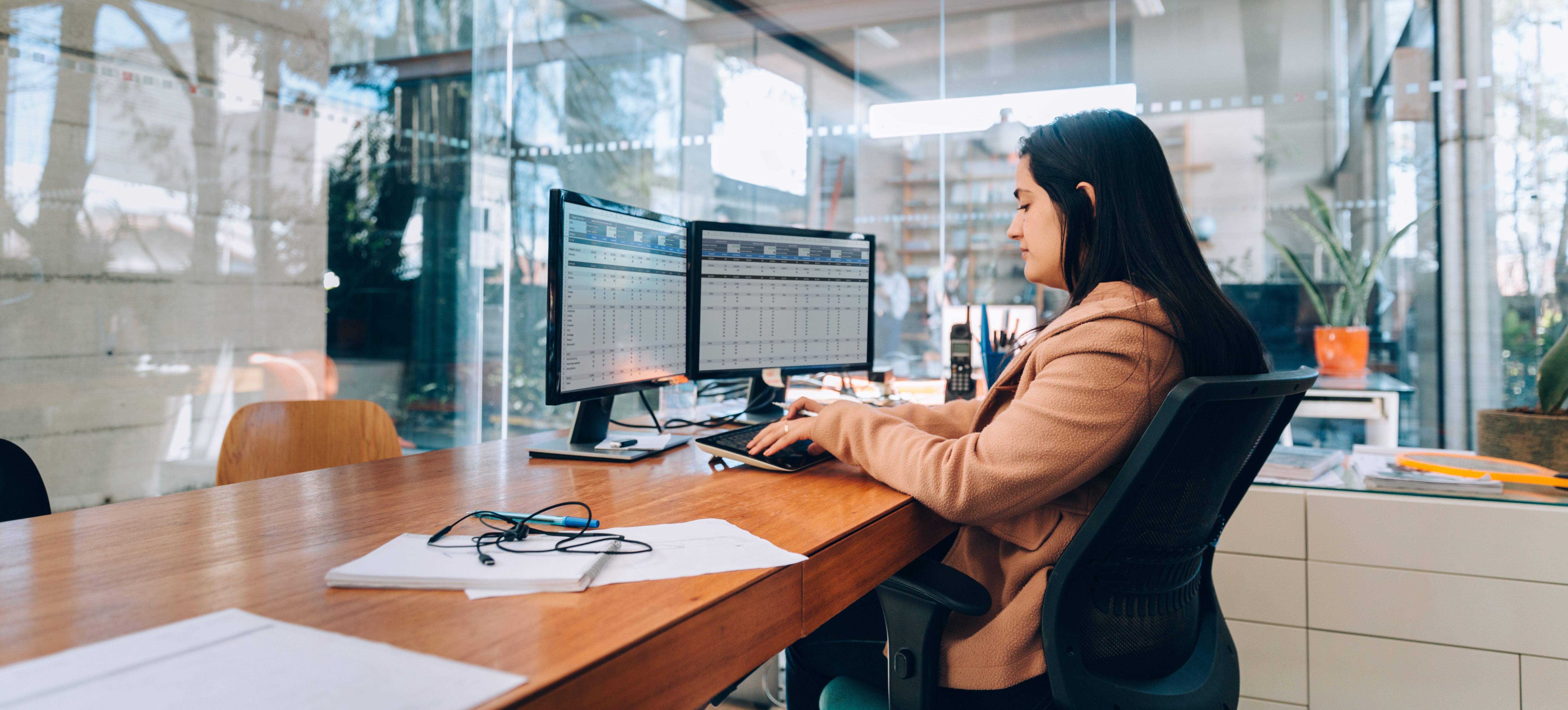 [Featured Image] A business person in an office with large glass walls uses Google Sheets automation on their computer.
