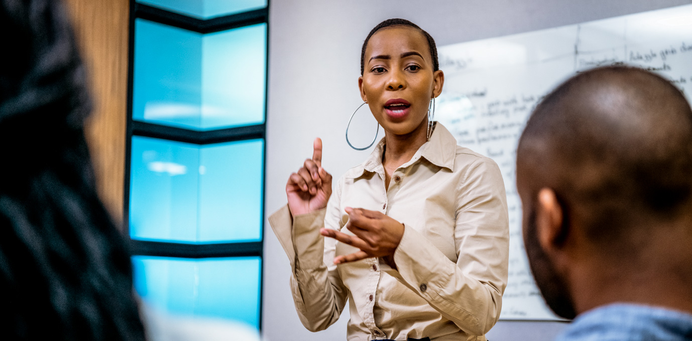 [Featured image] A person in organizational leadership speaking with authority in front of audience of organizational leadership degree students.