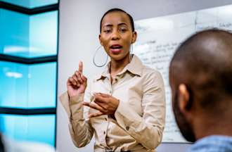 [Featured image] A woman in organizational leadership speaking with authority in front of audience of organizational leadership degree students.