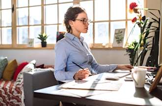 [Featured image] A UI designer with glasses on sits in front of a computer while sketching on a piece of paper.