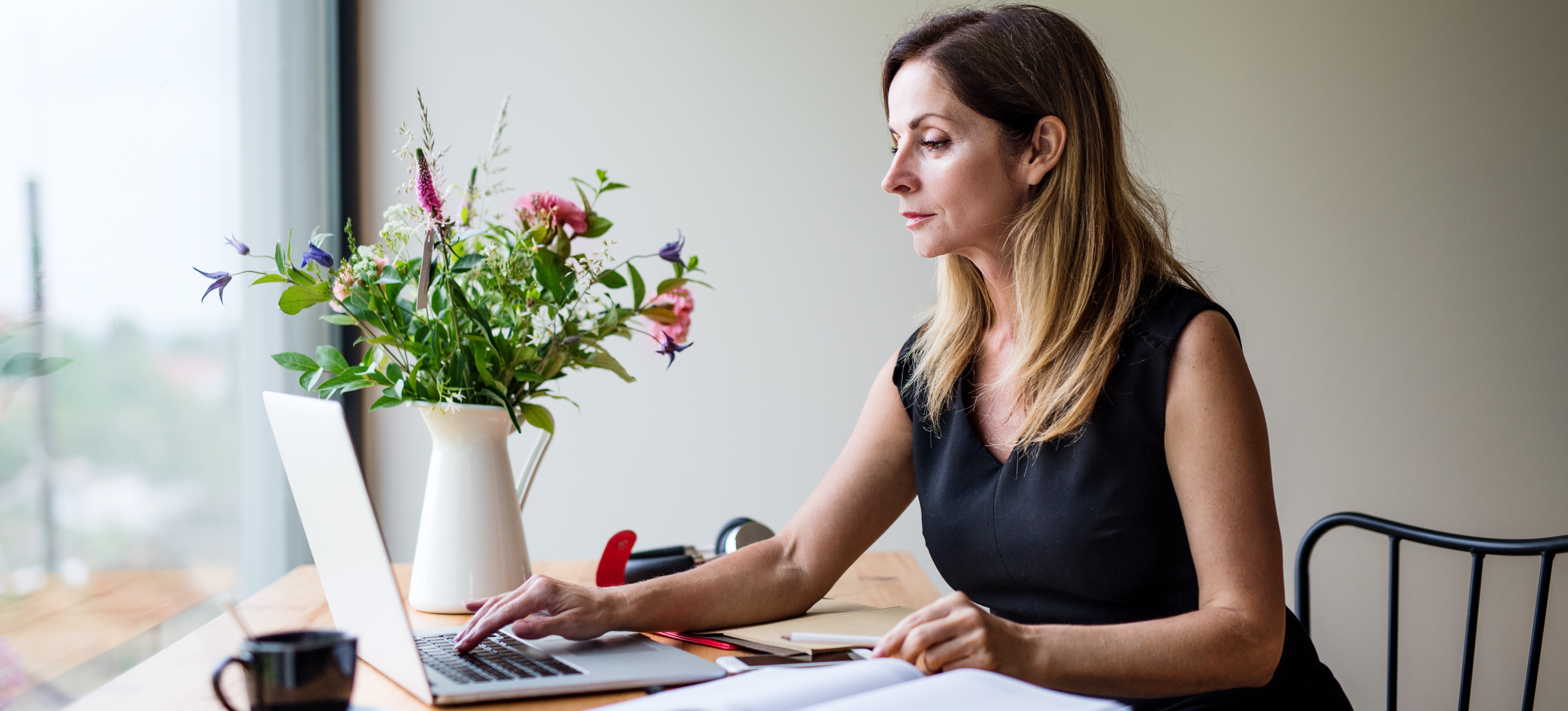 [Featured image] An MBA student attends a lecture on their laptop computer, sitting at a table next to a window.