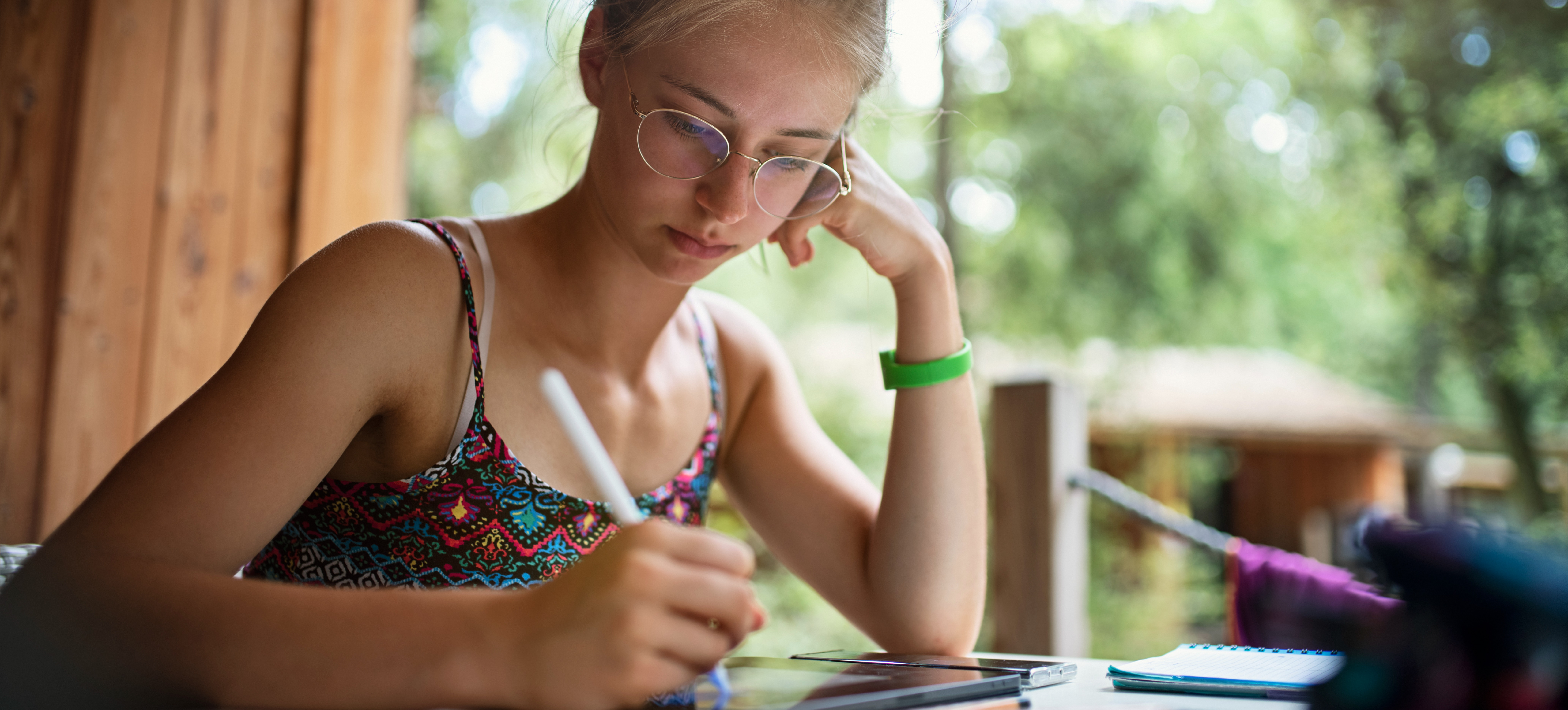 [Featured Image] A young woman is sitting at a desk making digital art by drawing on an tablet with a digital pen.