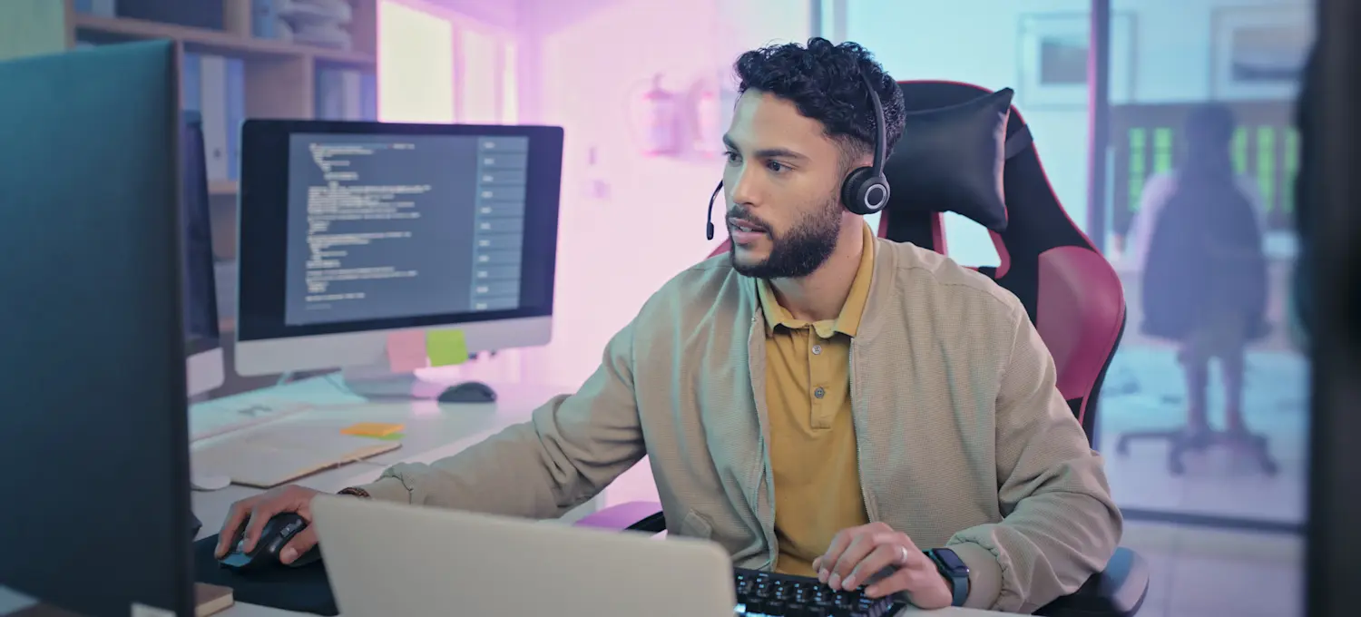 [Featured Image] A cloud security engineer sitting at a desk with several computer monitors in their office, wearing a headset and working intently at their job.