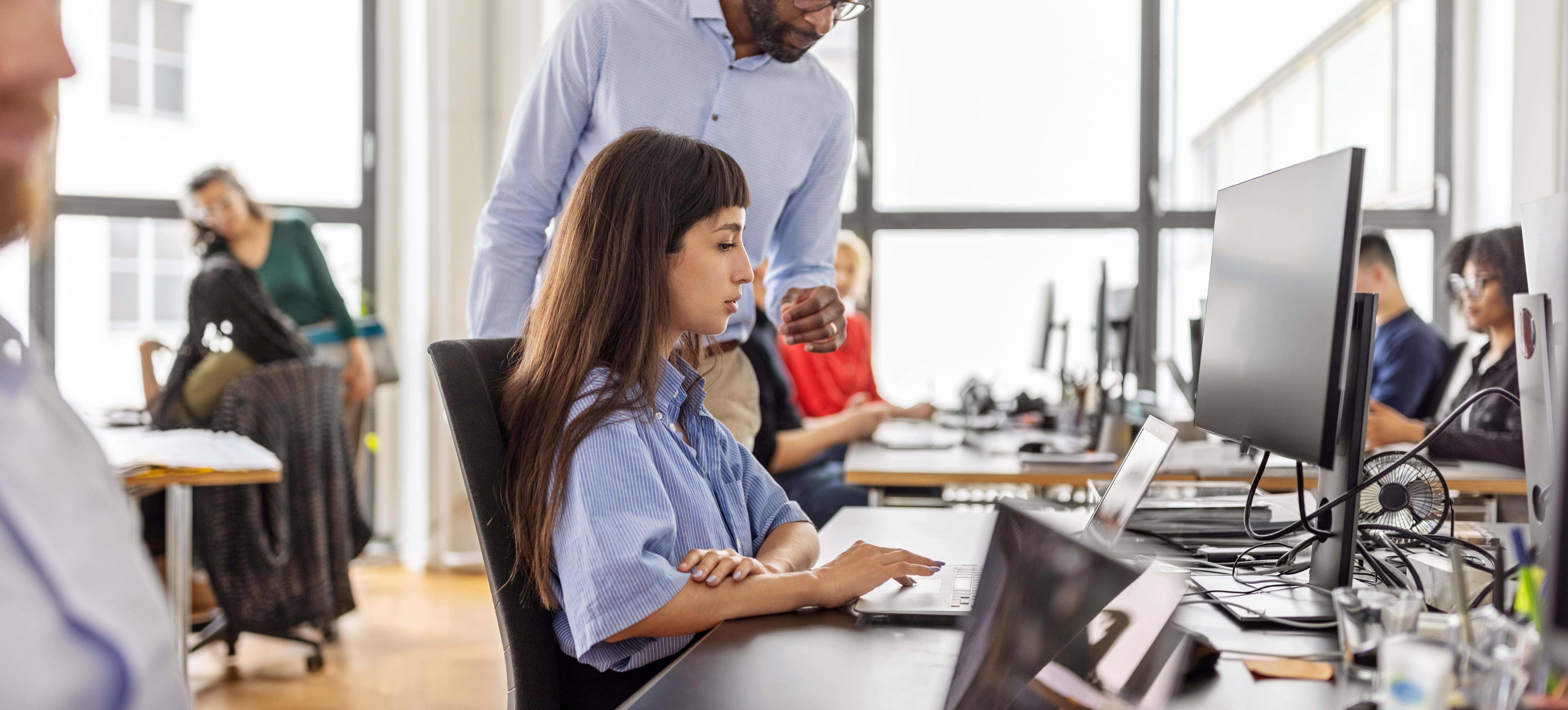 [Feature Image]: An instructor checks the work of a learner working to develop their skills in conducting sentiment analysis in Python in a computer lab with other learners.
