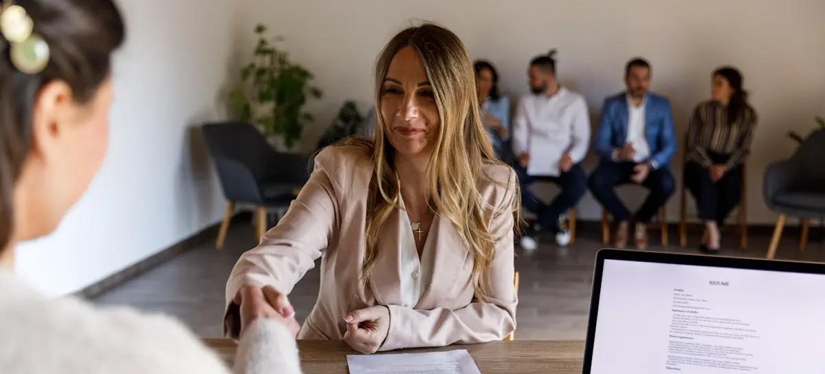 [Featured Image] A recruiter shakes hands with a candidate during an interview in a professional environment, with a predictive analytics resume visible on the table.
