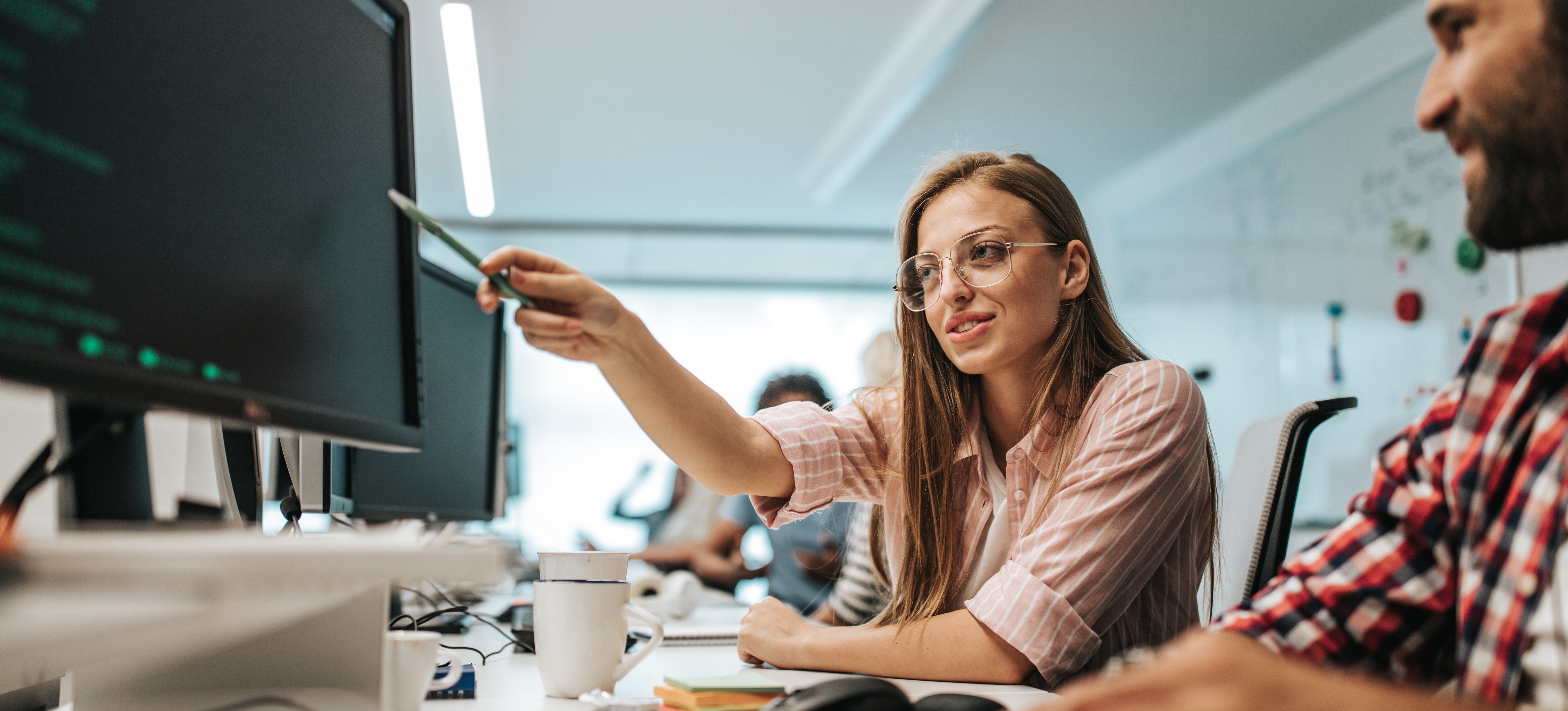 [Featured Image] Professionals in a work environment discussing DevOps vs. CI/CD while looking at a computer with code.
