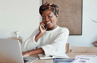 [Featured Image] A programmer sits at home, talks on the phone, and uses her laptop to research ads for R programming jobs. 
