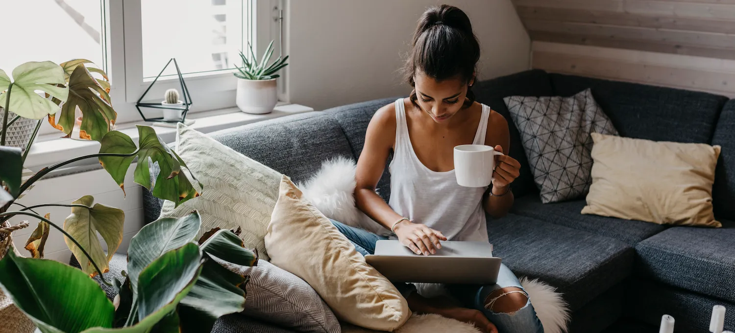 [Featured image] A person sits on a couch, holding a white mug, as they type a data analyst cover letter on their laptop.