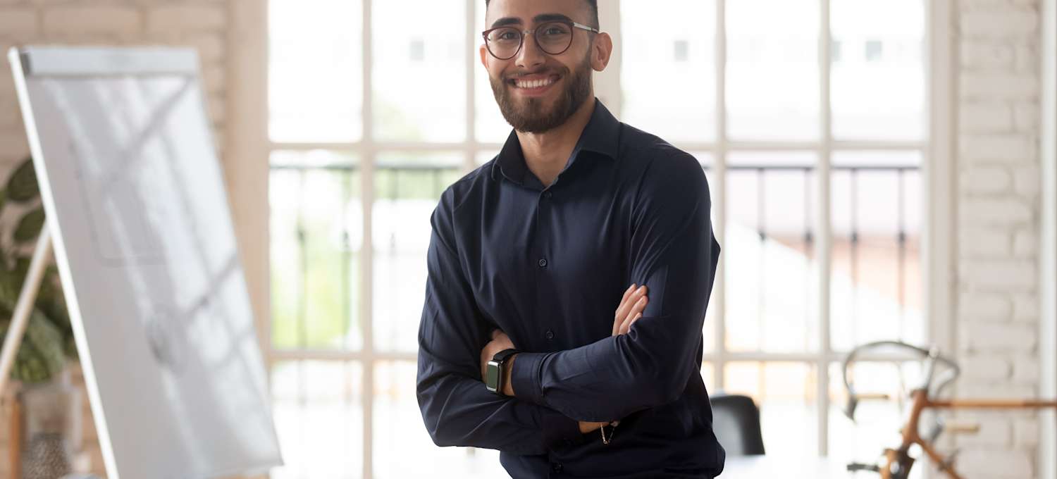 [Image] A man in a black button-up shirt stands in front of a window. 