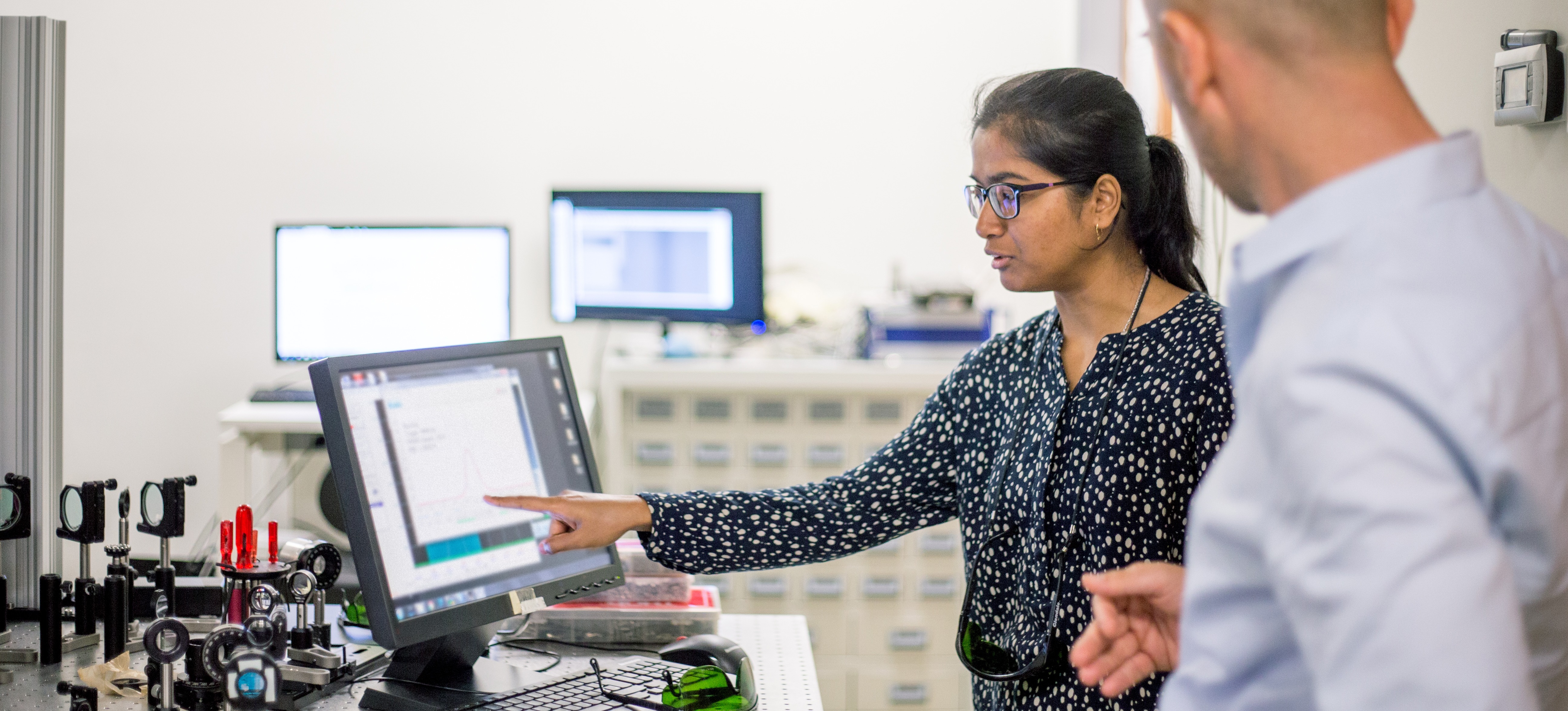 [Featured Image] A data engineer points to a computer while talking to a colleague about their machine learning jobs. 