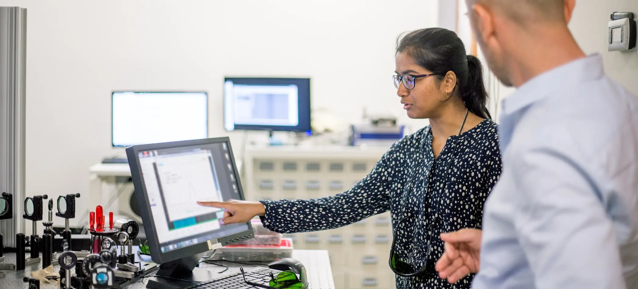[Featured Image] A data engineer points to a computer while talking to a colleague about their machine learning jobs. 