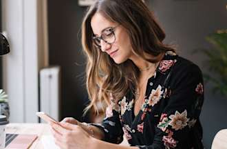 [Featued image] A woman is researching about the different routers on her phone while sitting at her desk. 