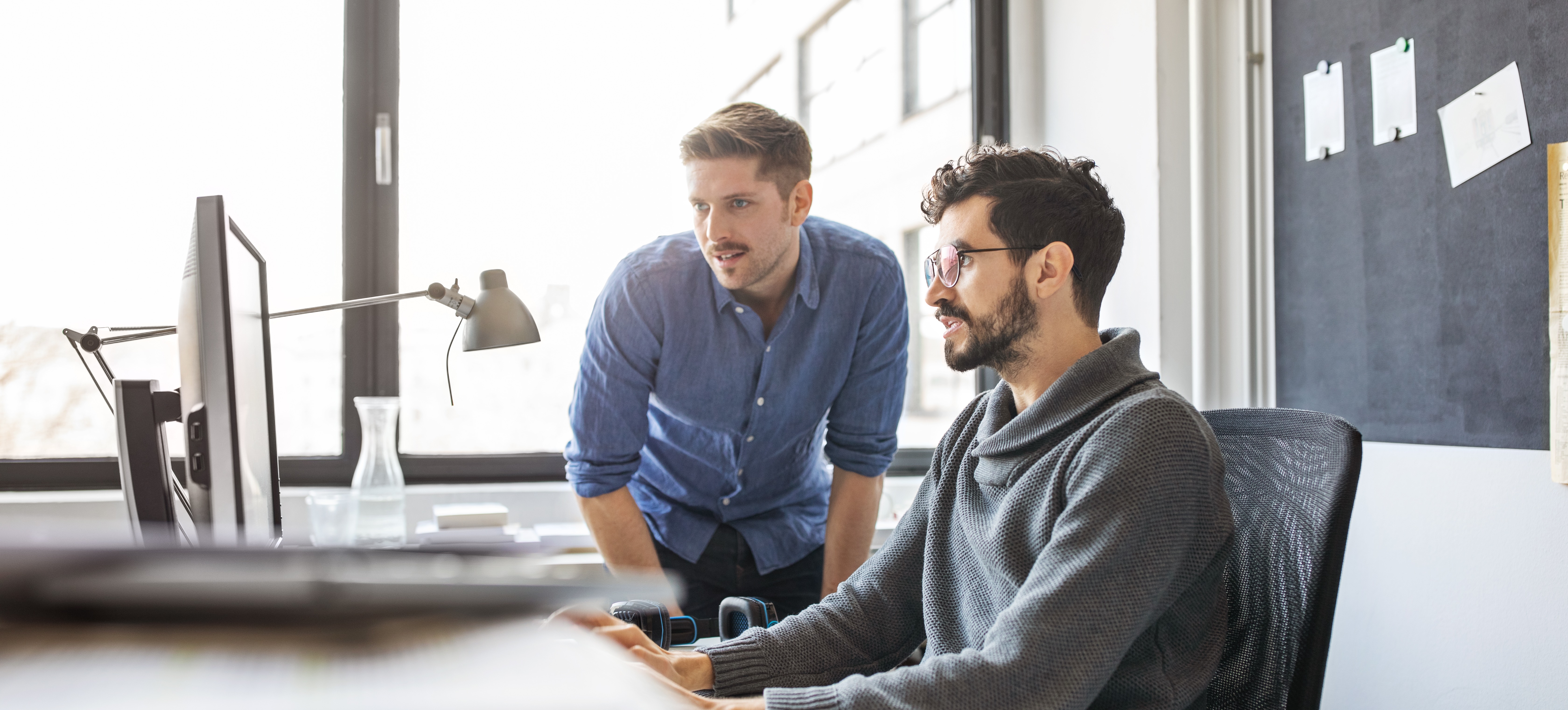 [Featured Image] Two IT professionals look at a computer and talk about their company's token ring.   