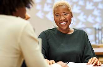 Une femme souriante aux cheveux courts et aux boucles d'oreilles est assise à une table lors d'un entretien d'embauche de designer UX
