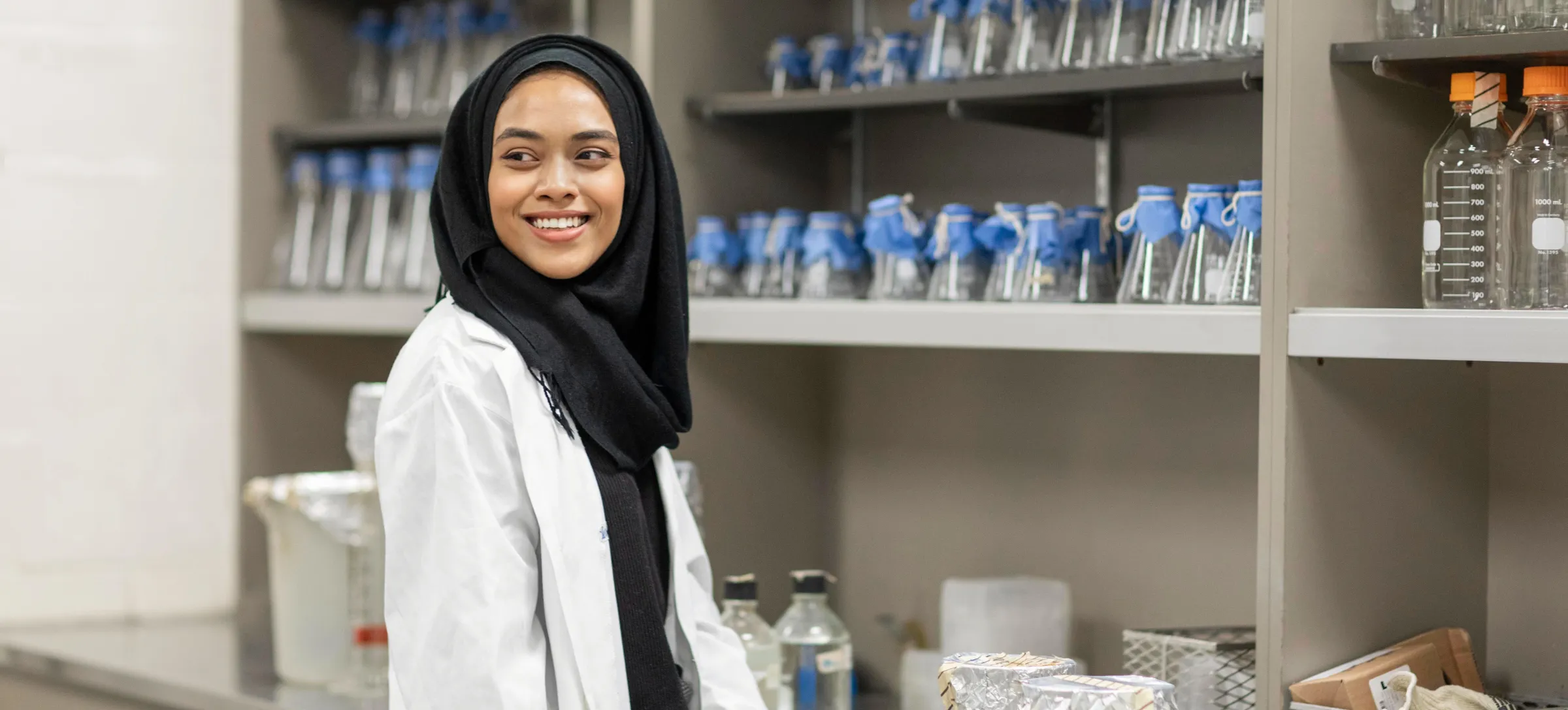 [Featured image] A chemist with a Master's in Chemistry stands in a laboratory near shelves of glass beakers.
