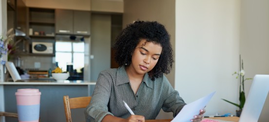 [Featured image]:  A woman is wearing a gray top, sitting at her desk in front of her laptop computer preparing her resume for a position in health care.