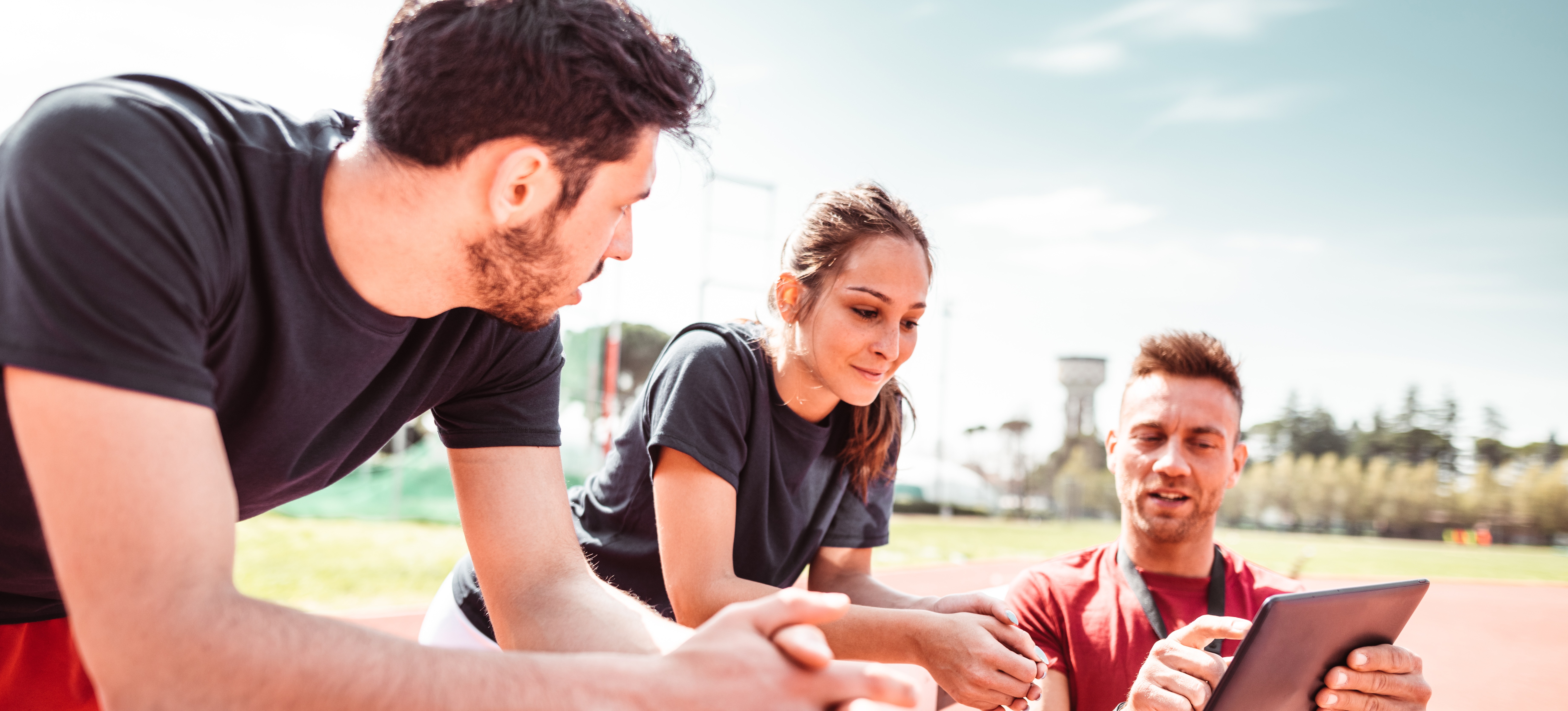 [Featured Image] A track and field coach, just one of the many available jobs in sports, talks to two runners on the track, pointing to a tablet.
