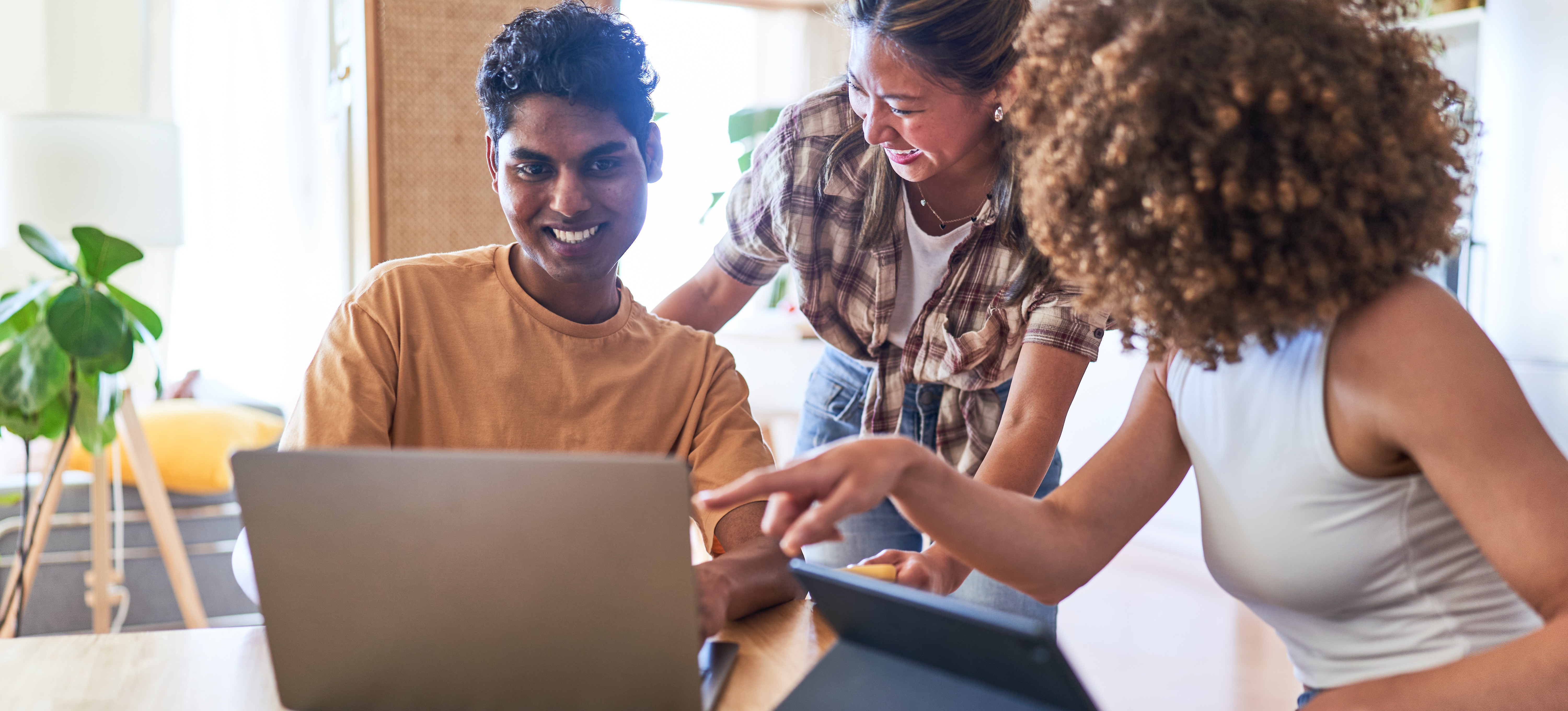 [Featured Image] Two learners gather around a third learner who is on their laptop as the trio explore health care data analyst careers and learn about the necessary qualifications. 