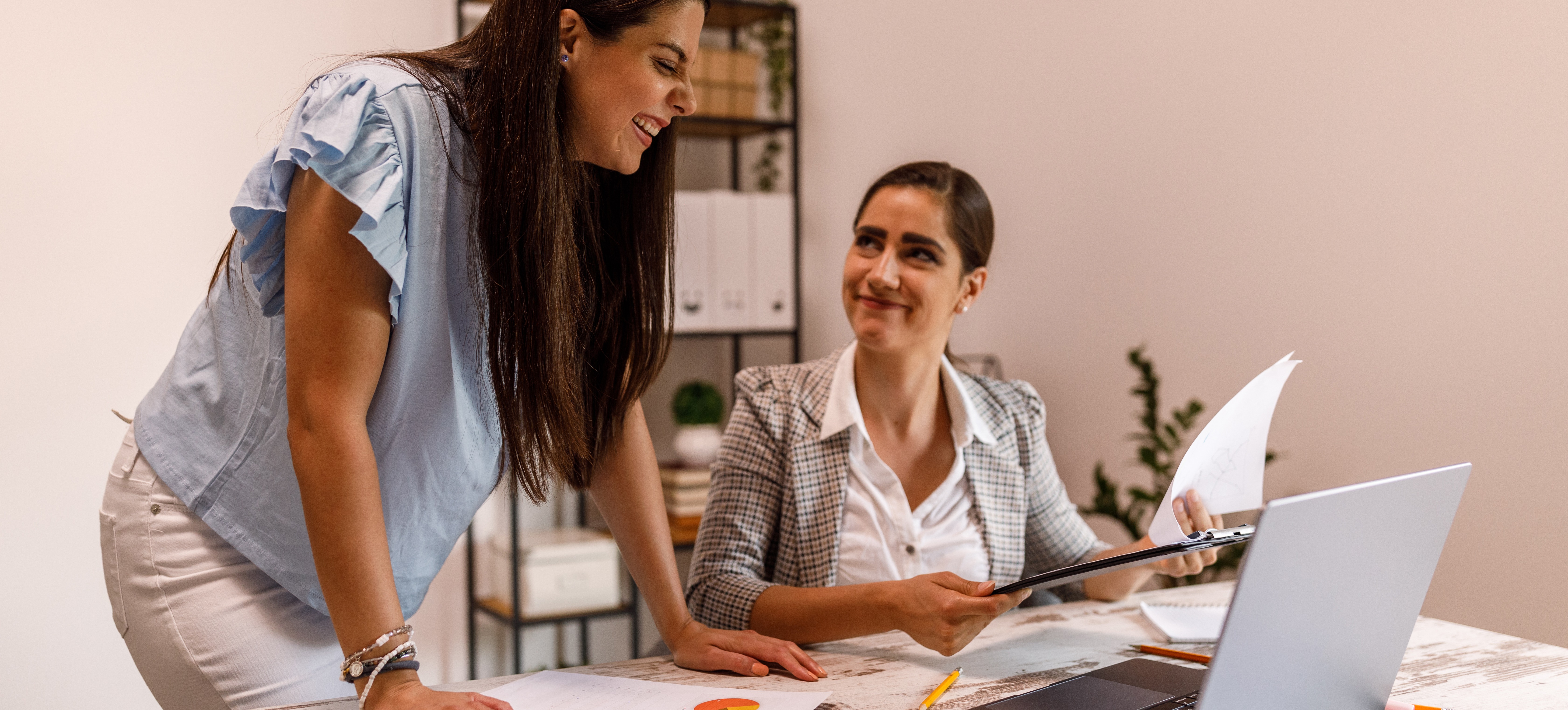 [Featured Image] A woman shows a colleague how to make a graph in Google Sheets on her laptop. 