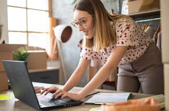 [Featured Image] A woman works on a laptop in a small store. 