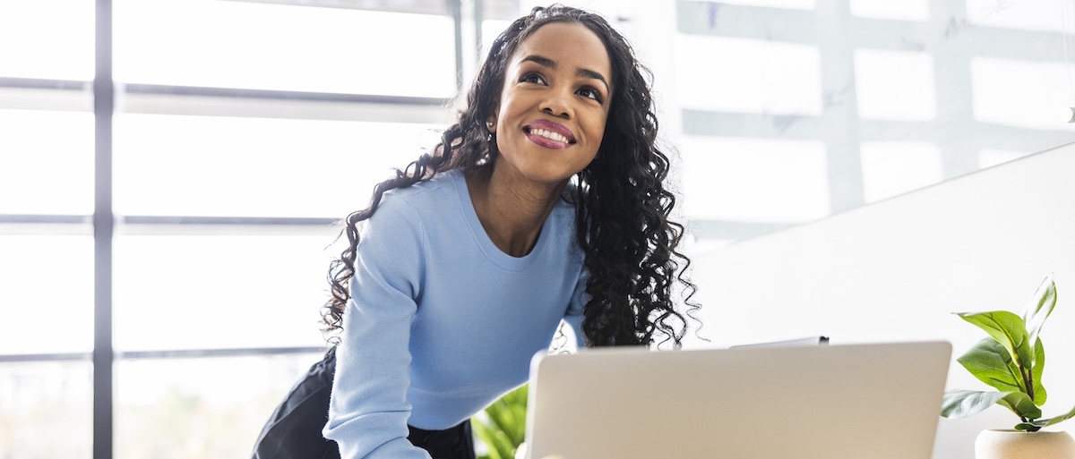[Featured image] A female project manager stands behind her laptop smiling. 