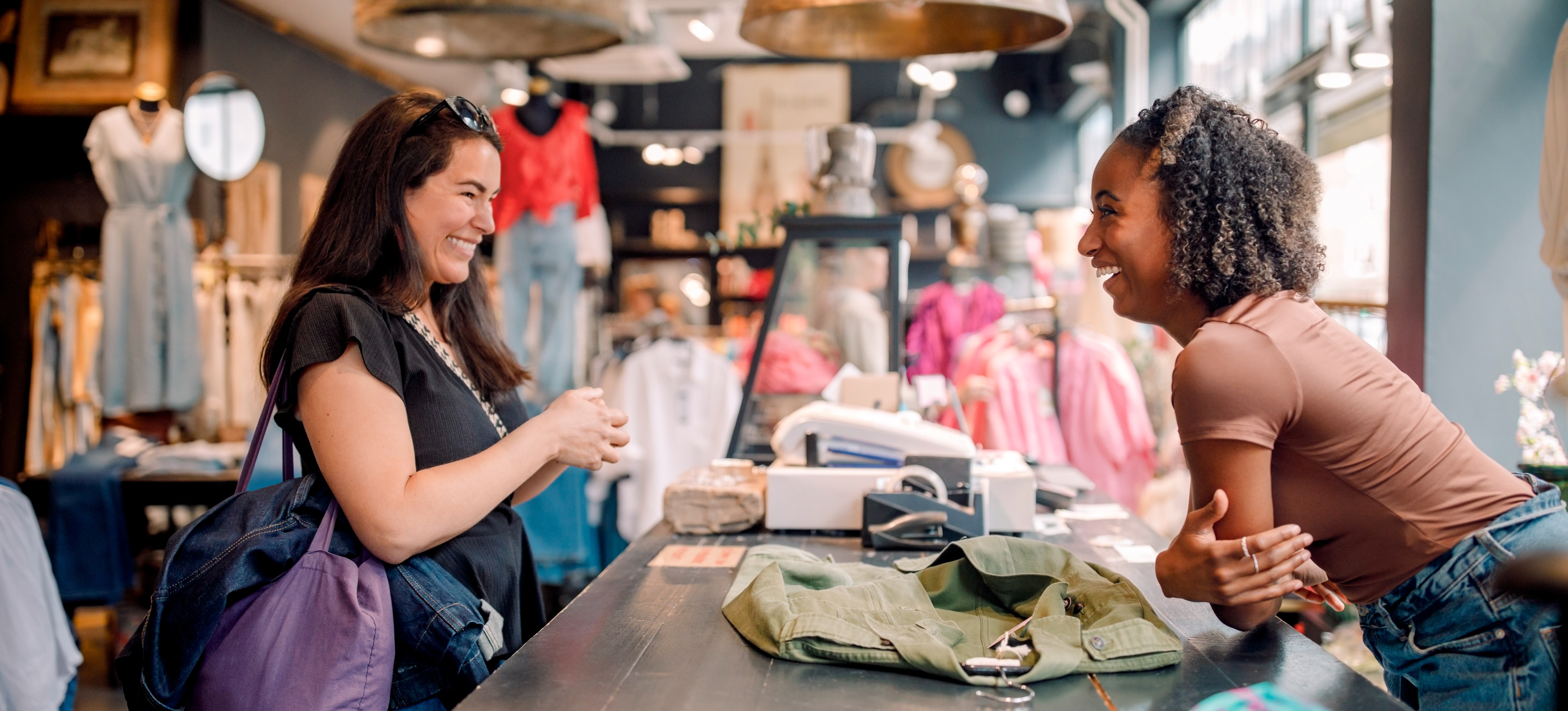 [Featured Image] A business owner who has learned how to apply a customer-centric approach to their business has a friendly conversation with a customer at the checkout counter. 
