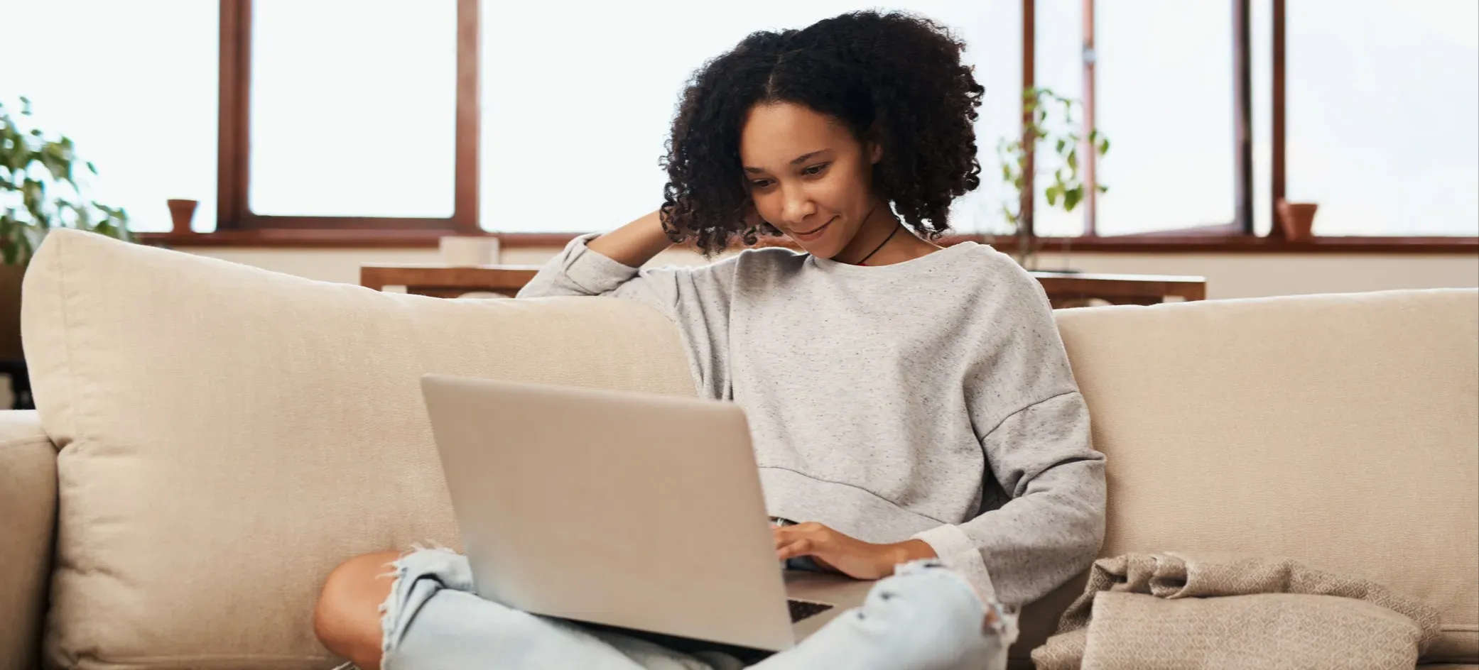 [Featured Image] Woman sitting on a couch using a laptop, comparing ChatGPT vs Gemini for writing, research, and everyday productivity tasks.