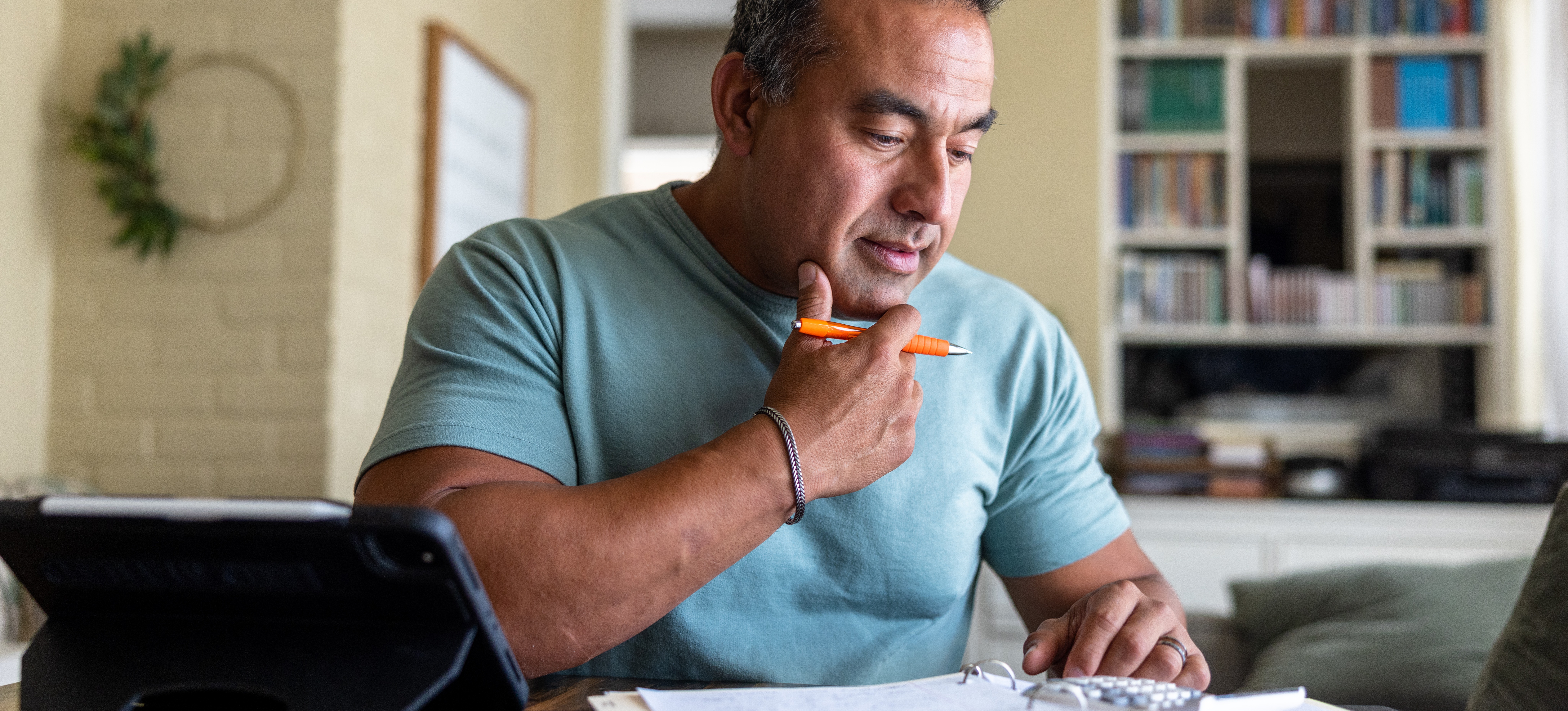 [Featured Image] An IT professional sits at a desk with his tablet and a notebook at home and studies for his Azure Fundamentals certification. 