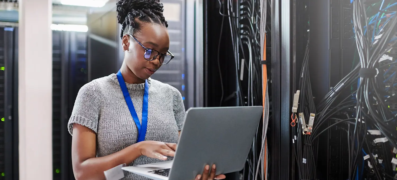 [Featured Image] A network engineer stands in a server room with a laptop looking at the physical layer mechanics
