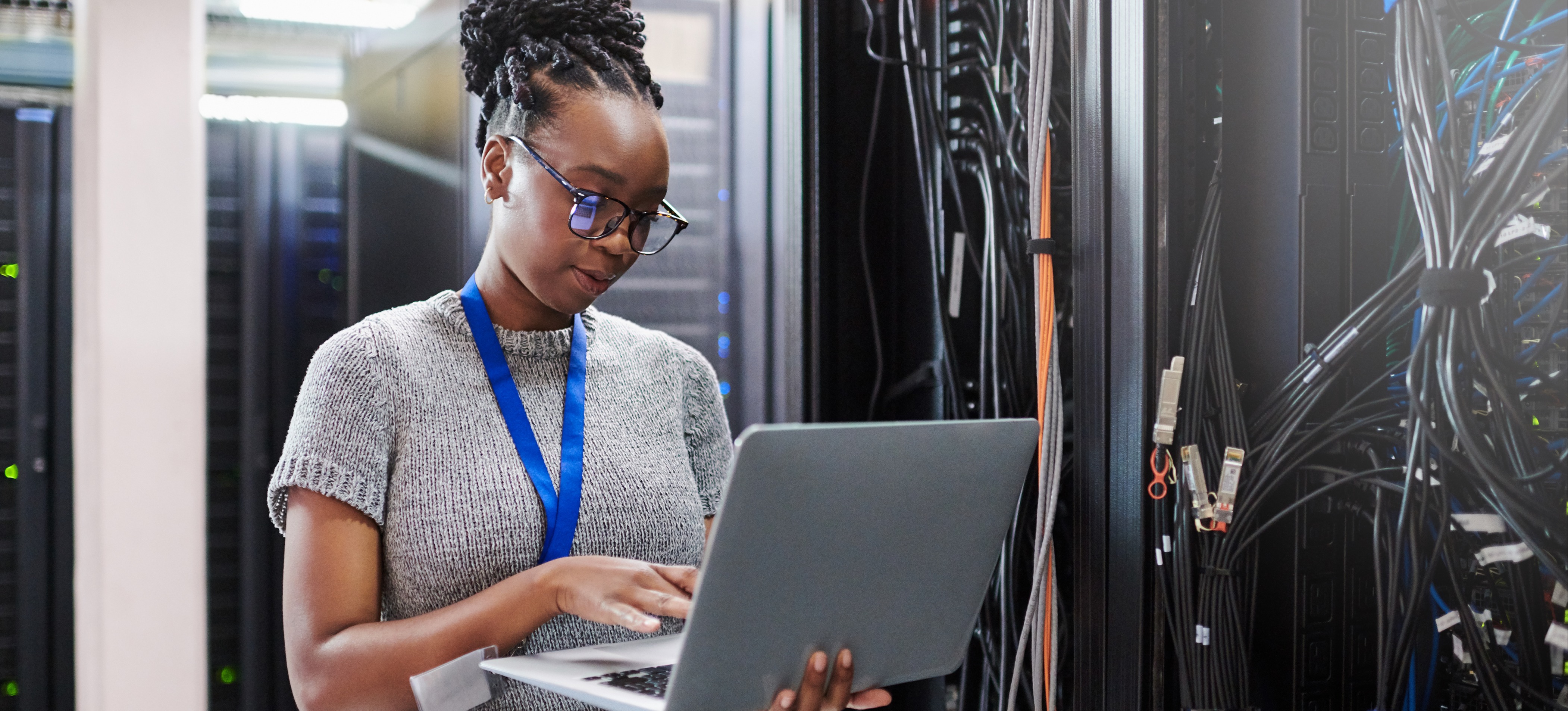 [Featured Image] A female network engineer stands in a server room with a laptop looking at the physical layer mechanics