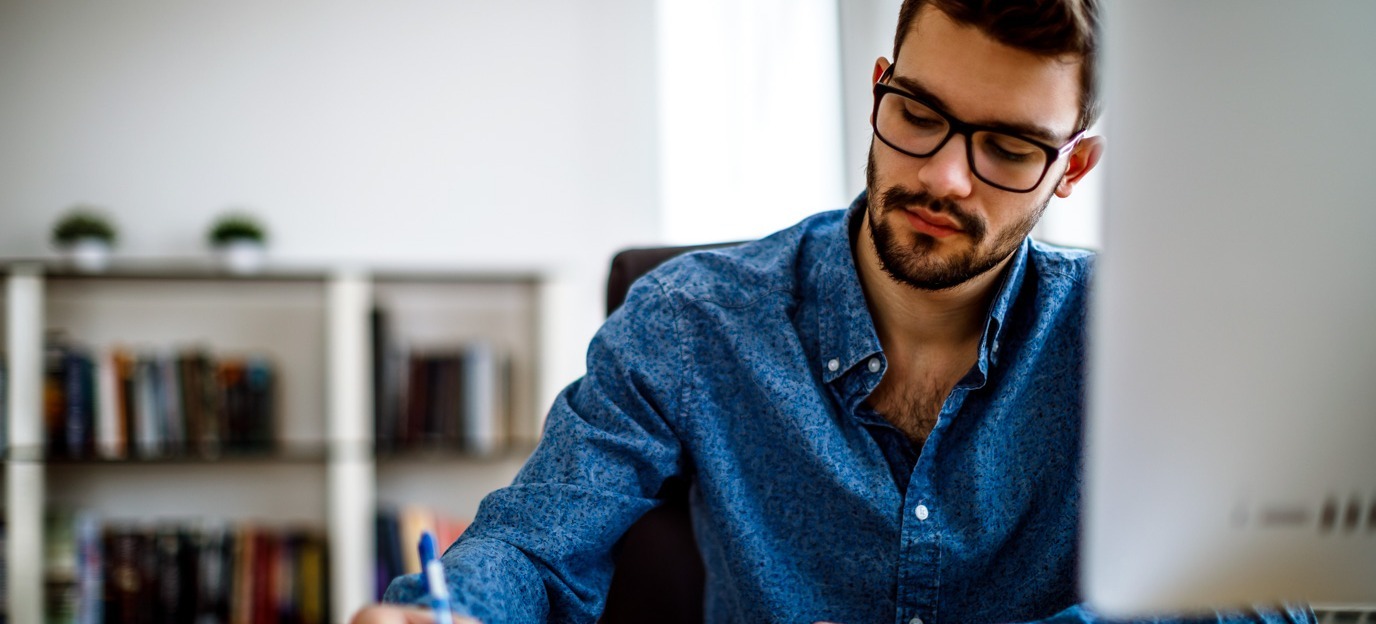[Imagen destacada] Hombre con gafas y camisa azul trabajando en su master delante de un ordenador.