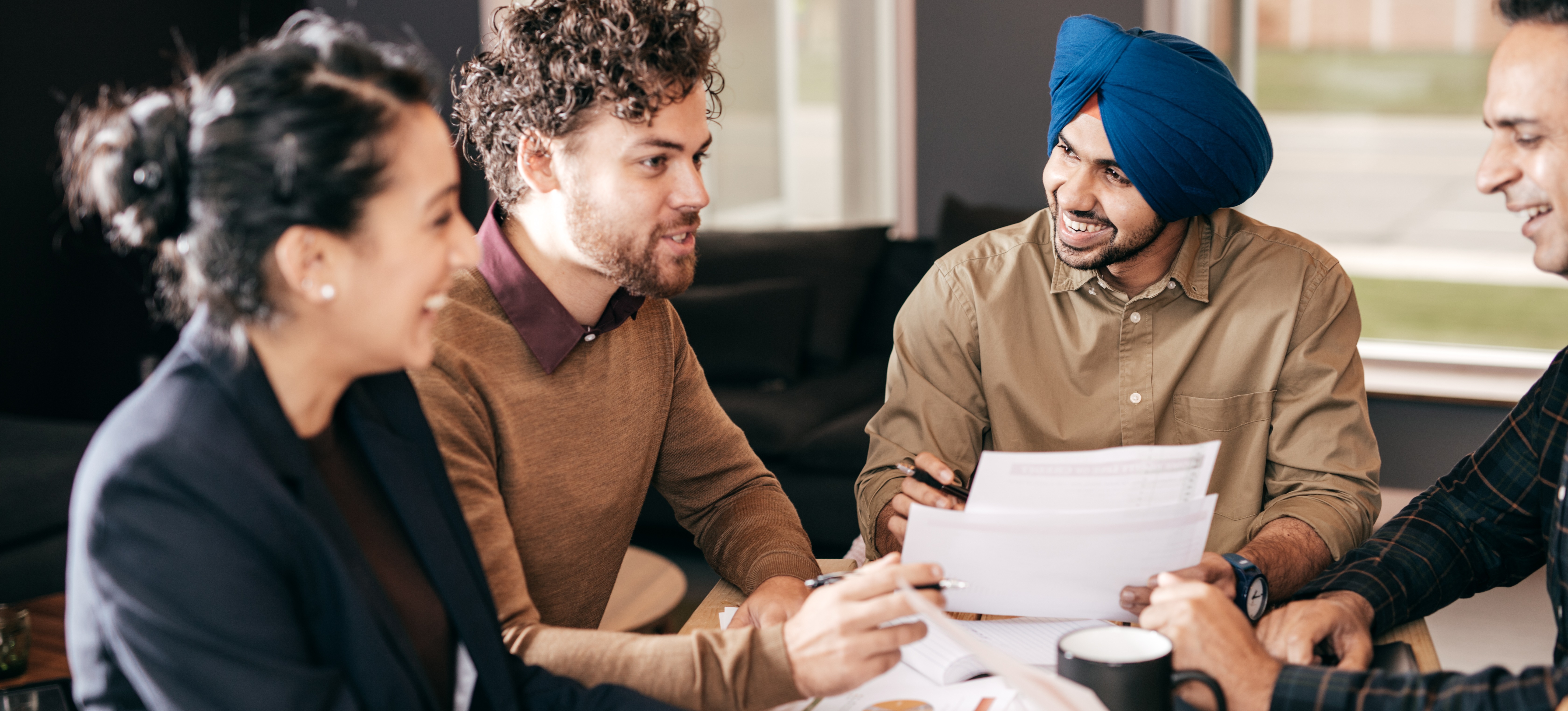 [Featured Image] Four learners excitedly discuss advertising agency services, jobs, training, and salaries as they plan their career paths. 
