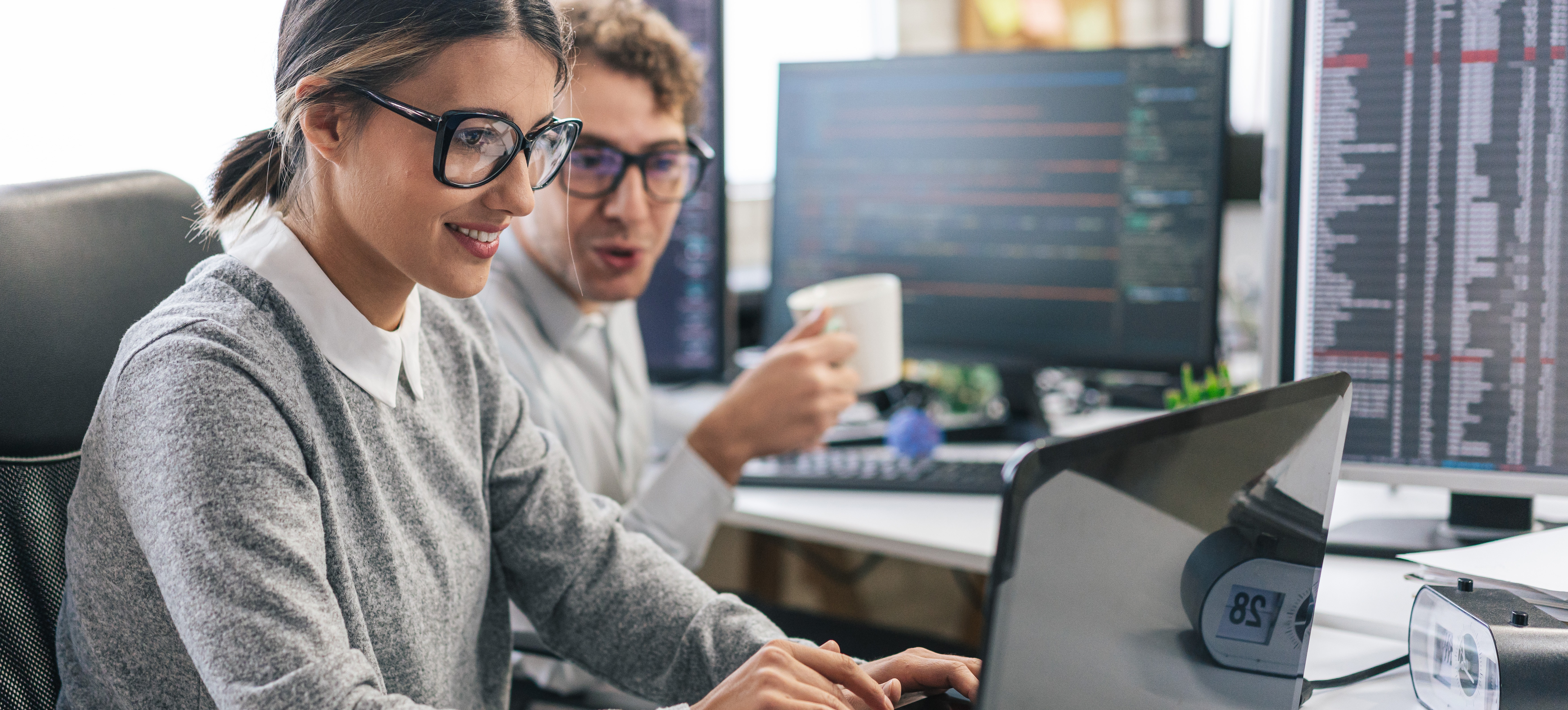 [Featured Image] Professionals in a workspace discuss how to improve C# programming skills while working with C# code on their computers.