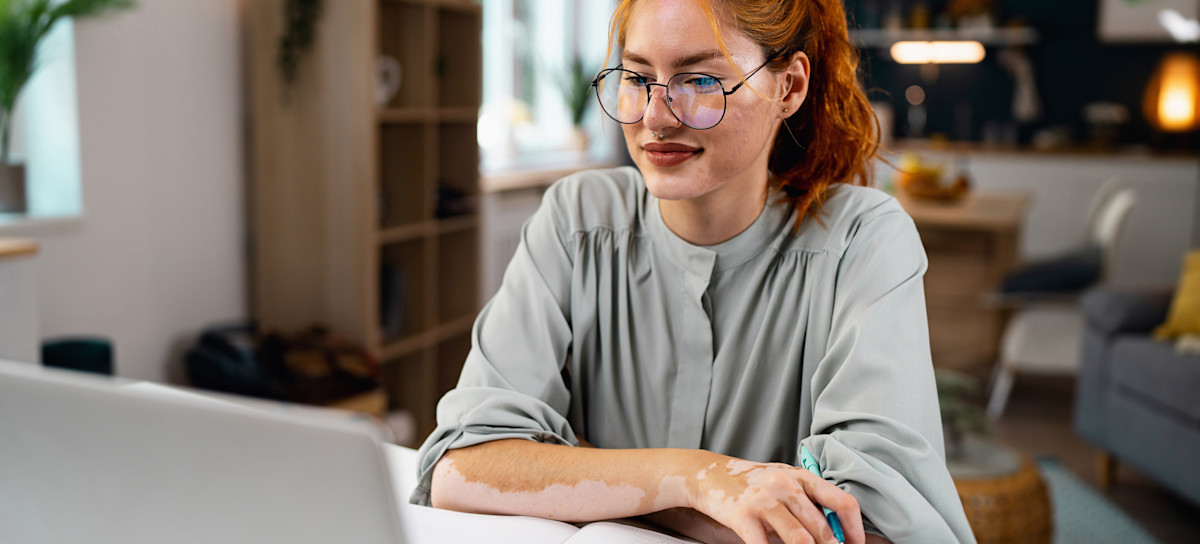 [Featured Image] A young woman sits at her computer and researches how to write a LinkedIn summary.