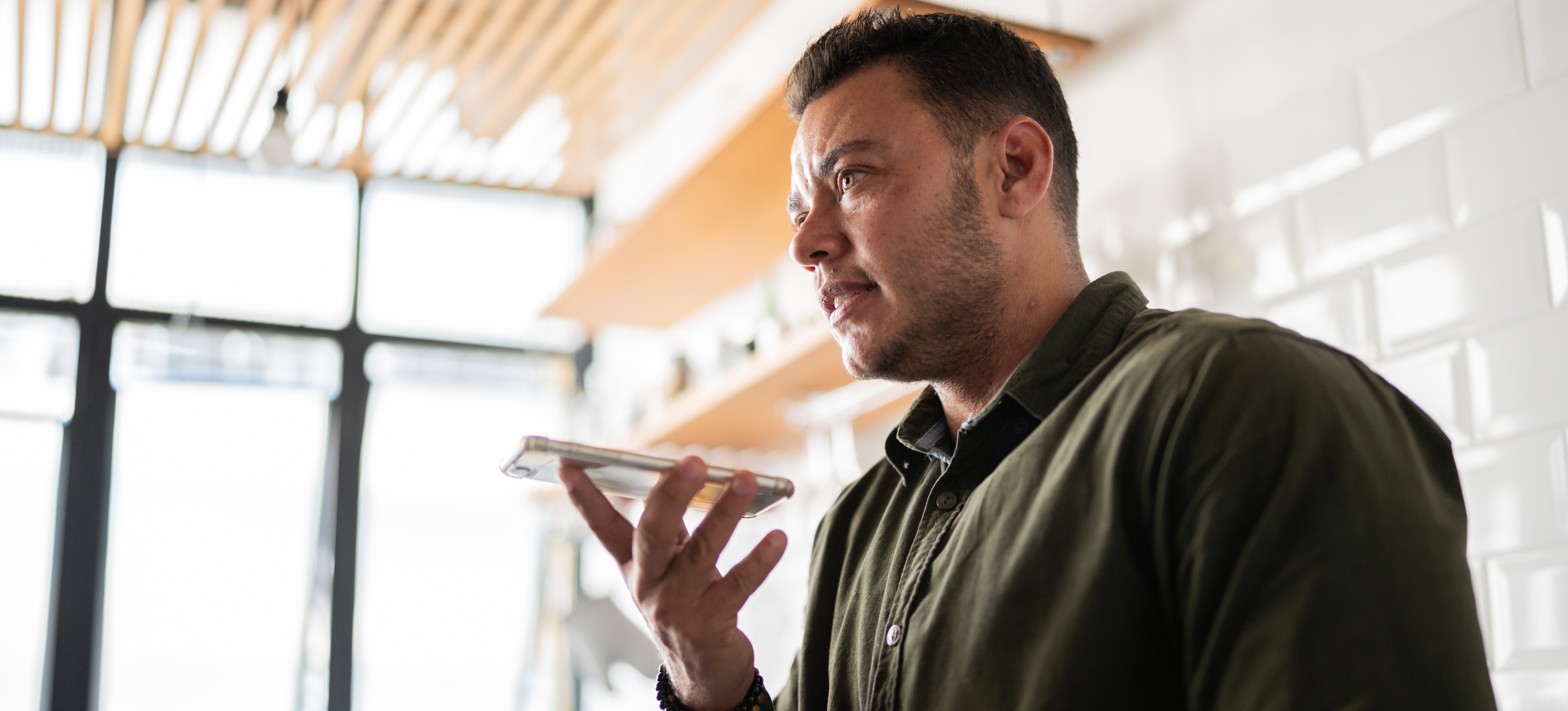 [Featured Image] A man in an office with large windows speaks into a smartphone, which uses syntax analysis to convert speech to text.
