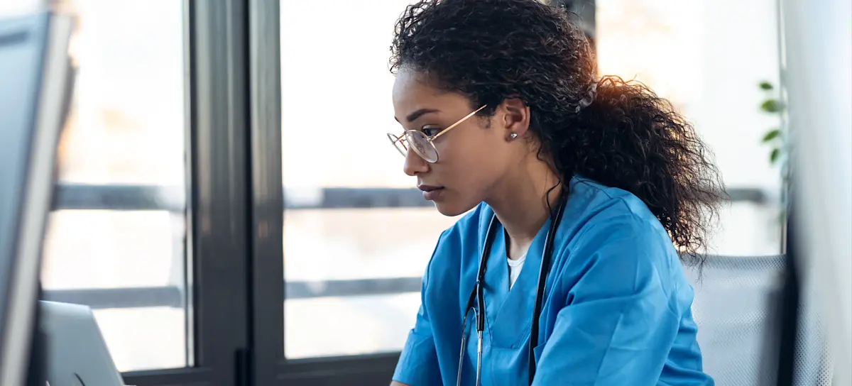 [Featured Image] A nurse practitioner wearing scrubs works on a laptop.