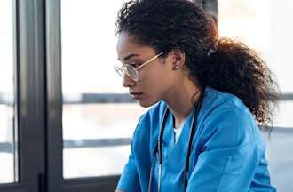 [Featured Image] A nurse wearing scrubs works on a laptop.