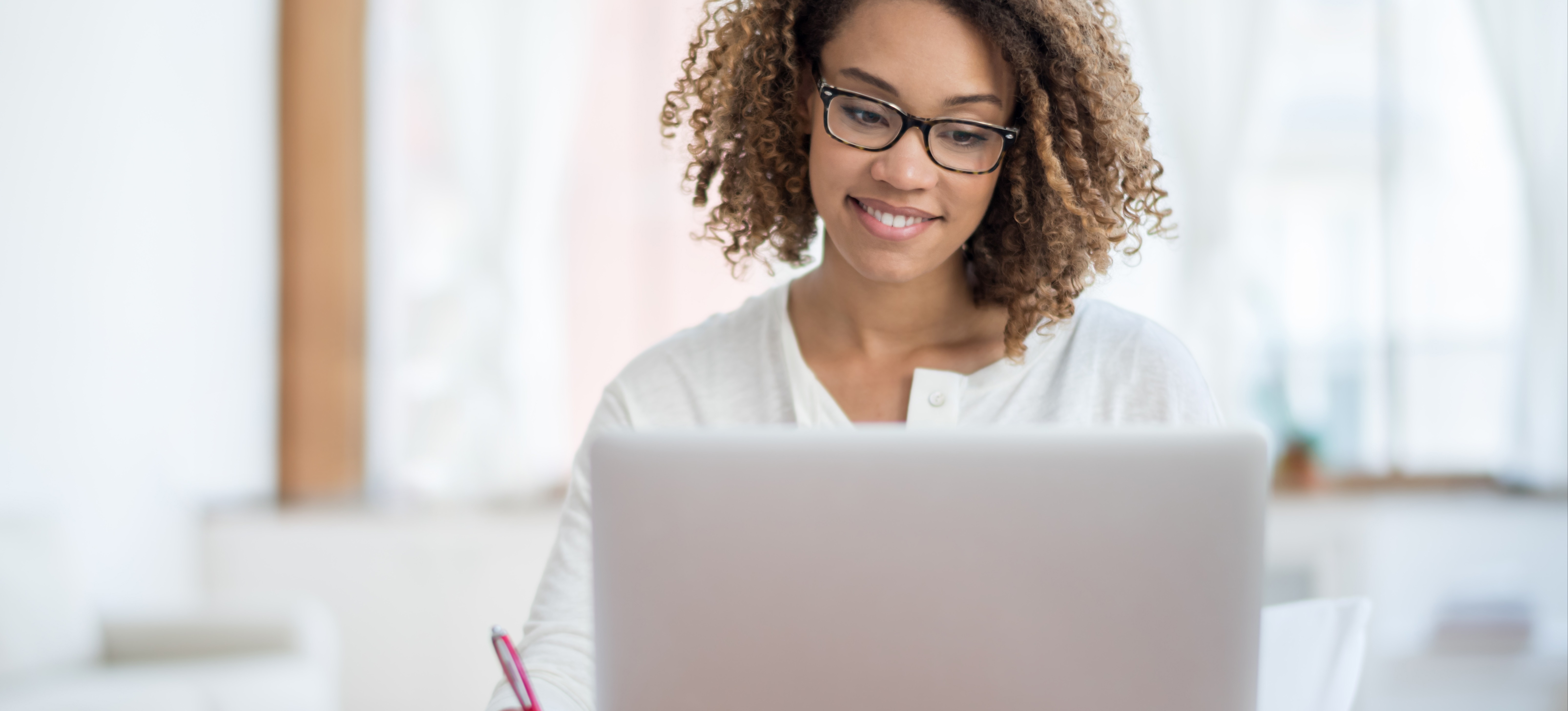[Hauptbild] Eine SEO-Spezialistin mit Brille arbeitet an ihrem Laptop an einem Schreibtisch, während sie in ein Notizbuch schreibt.
