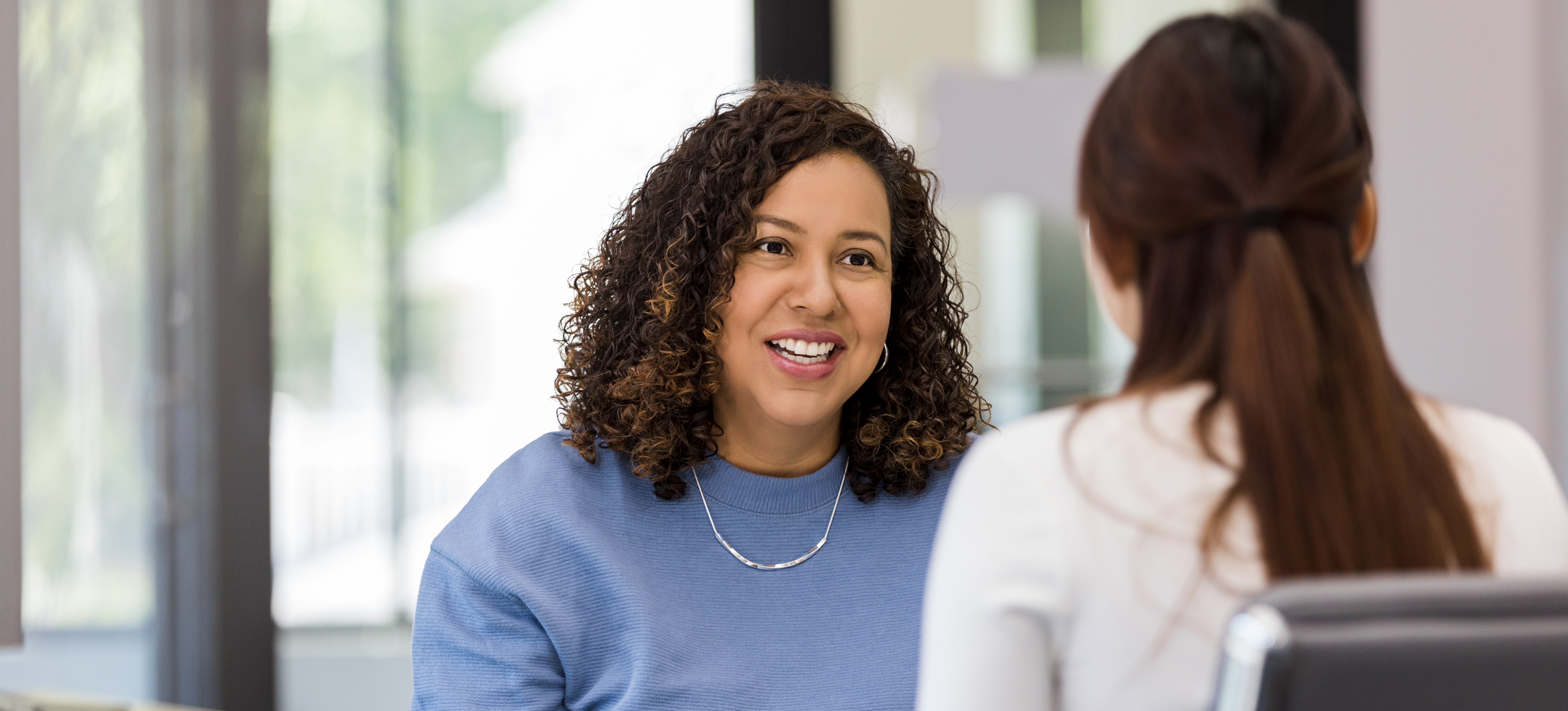 [Featured Image] An HR specialist takes notes and talks to a new employee as she helps her human resources department with the onboarding process. 
