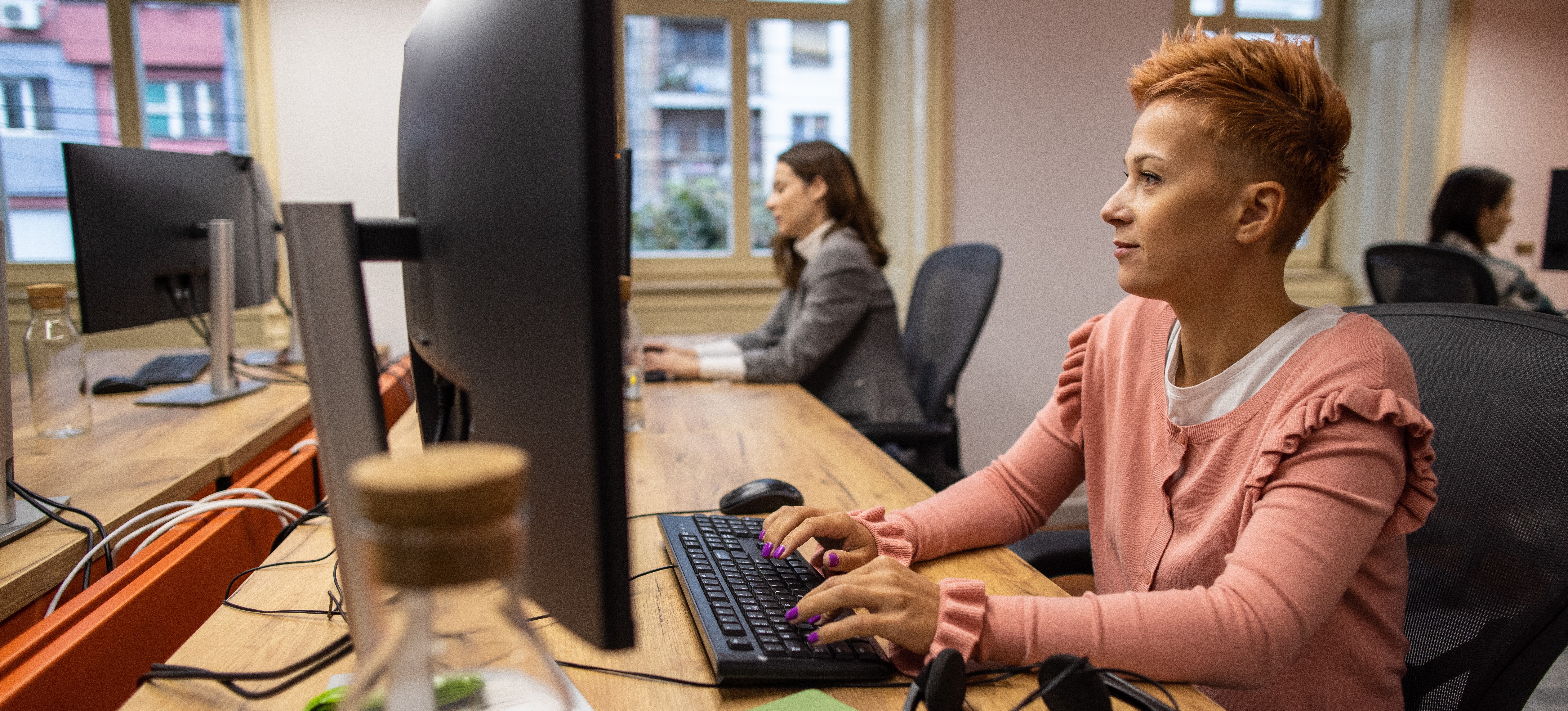 [Hauptbild] Eine Frau an einem Computertisch in einem Büro, das ein Peer-to-Peer-Netzwerk für alle anderen Computer und Drucker nutzt.