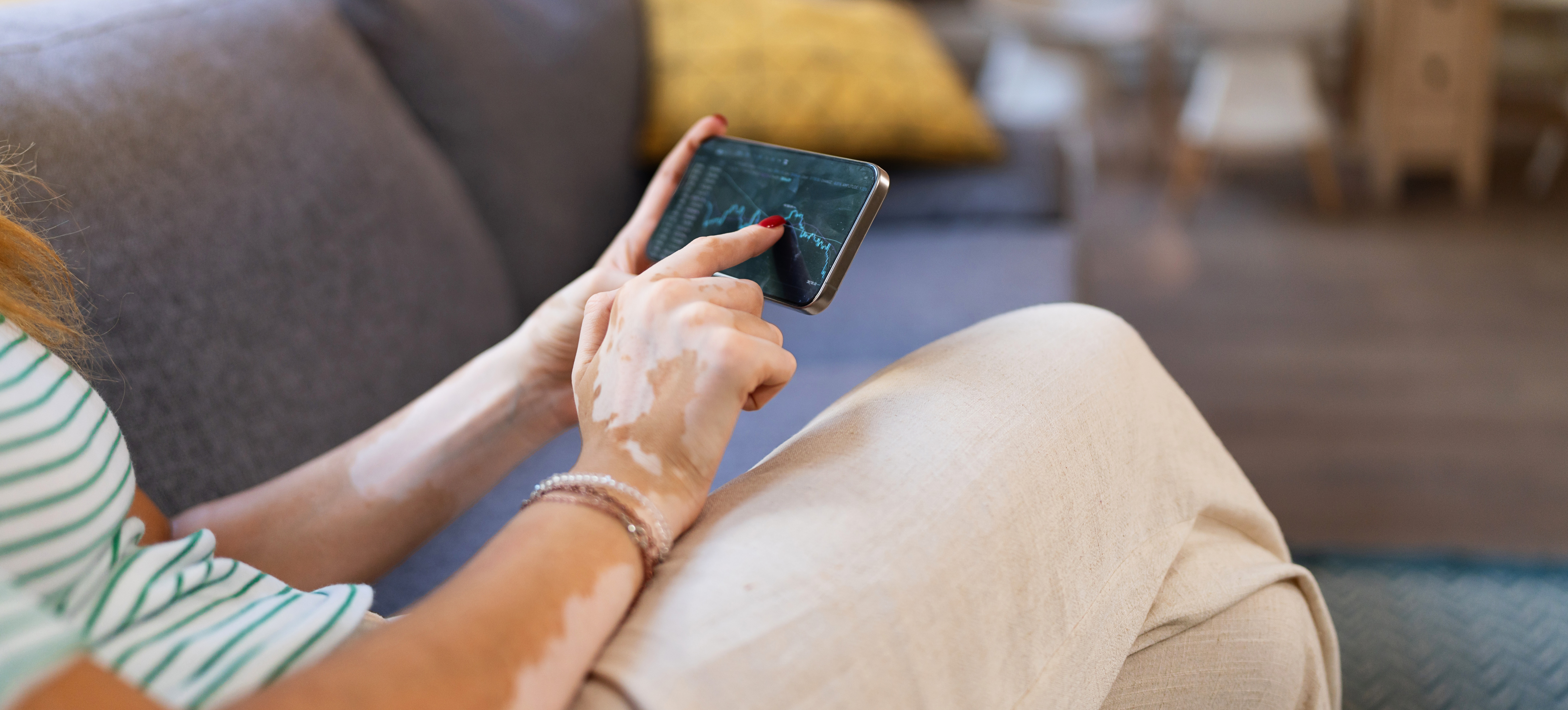 [Featured Image] A woman on her phone is trading cryptocurrency at her house.