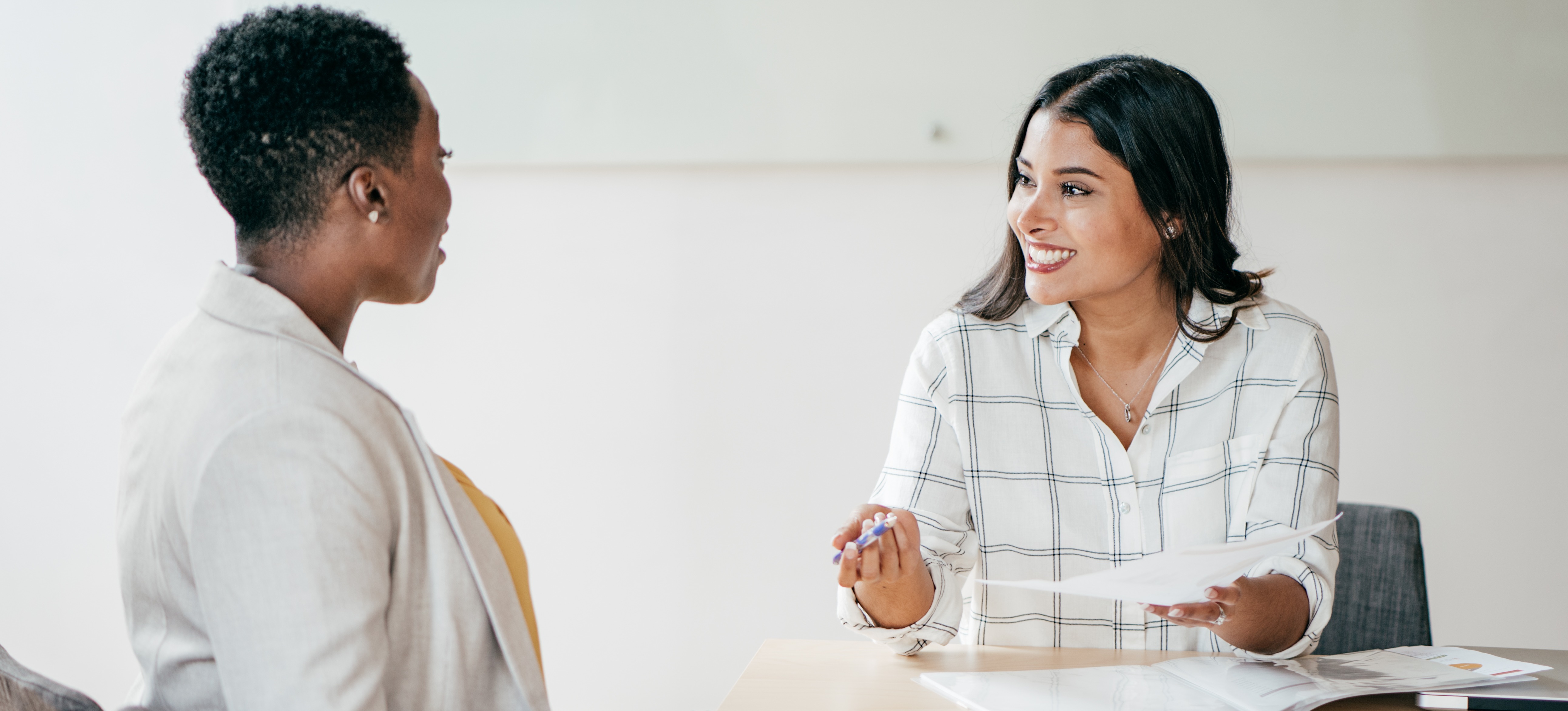 [Featured Image] A woman earning a human resources salary talks with another businesswoman during a job interview at a conference table.
