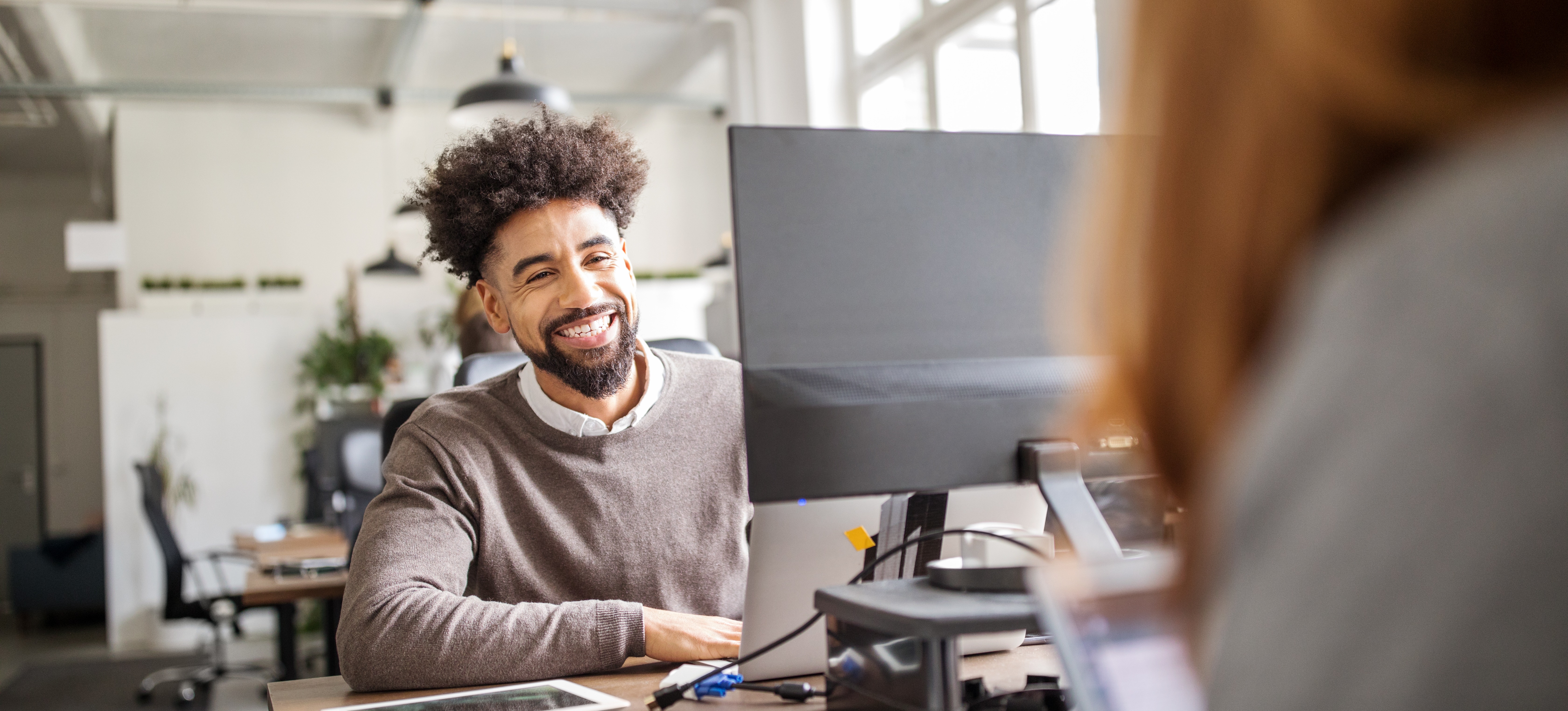 [Featured Image] After debating a computer science vs software engineering career path, a smiling person works at a laptop in a bright and airy open concept office.

