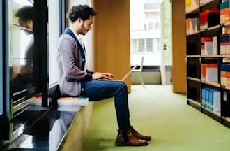 Featured image: A person works on their laptop in a library filled with books, researching an MA vs. MS degree.